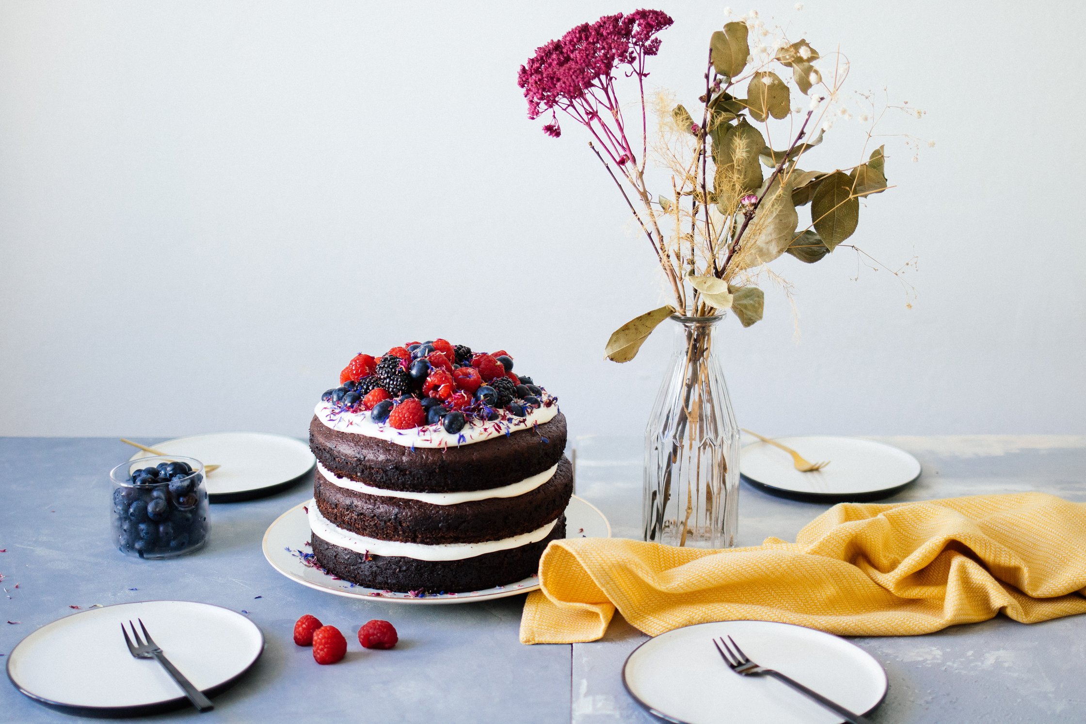 vegane Torte ist neben Tellern und Blumen auf einem blauen Untergrund platziert