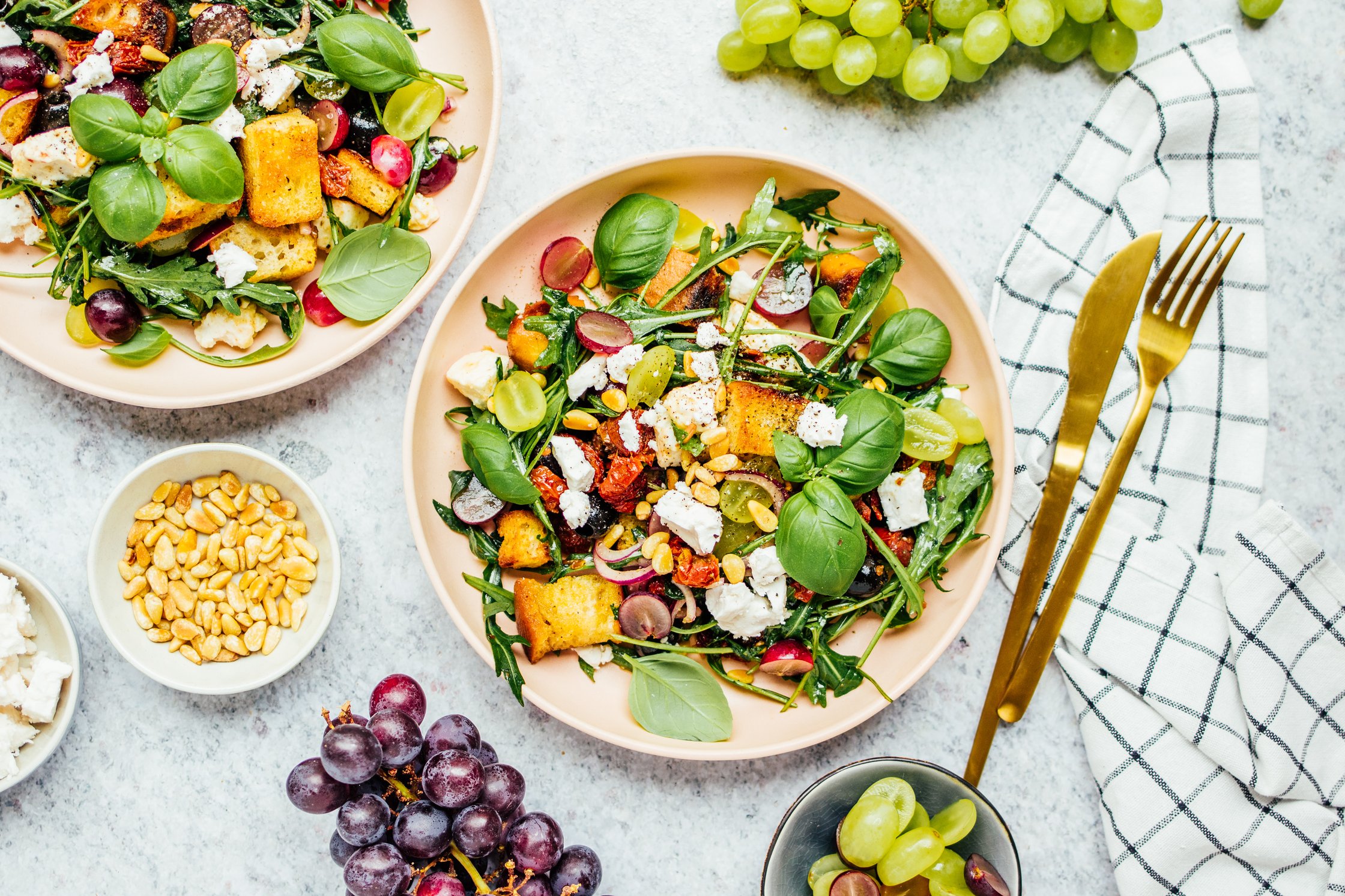 veganer Frühlings Brotsalat angerichtet auf Teller mit veganem Feta und gerösteten Pinienkernen