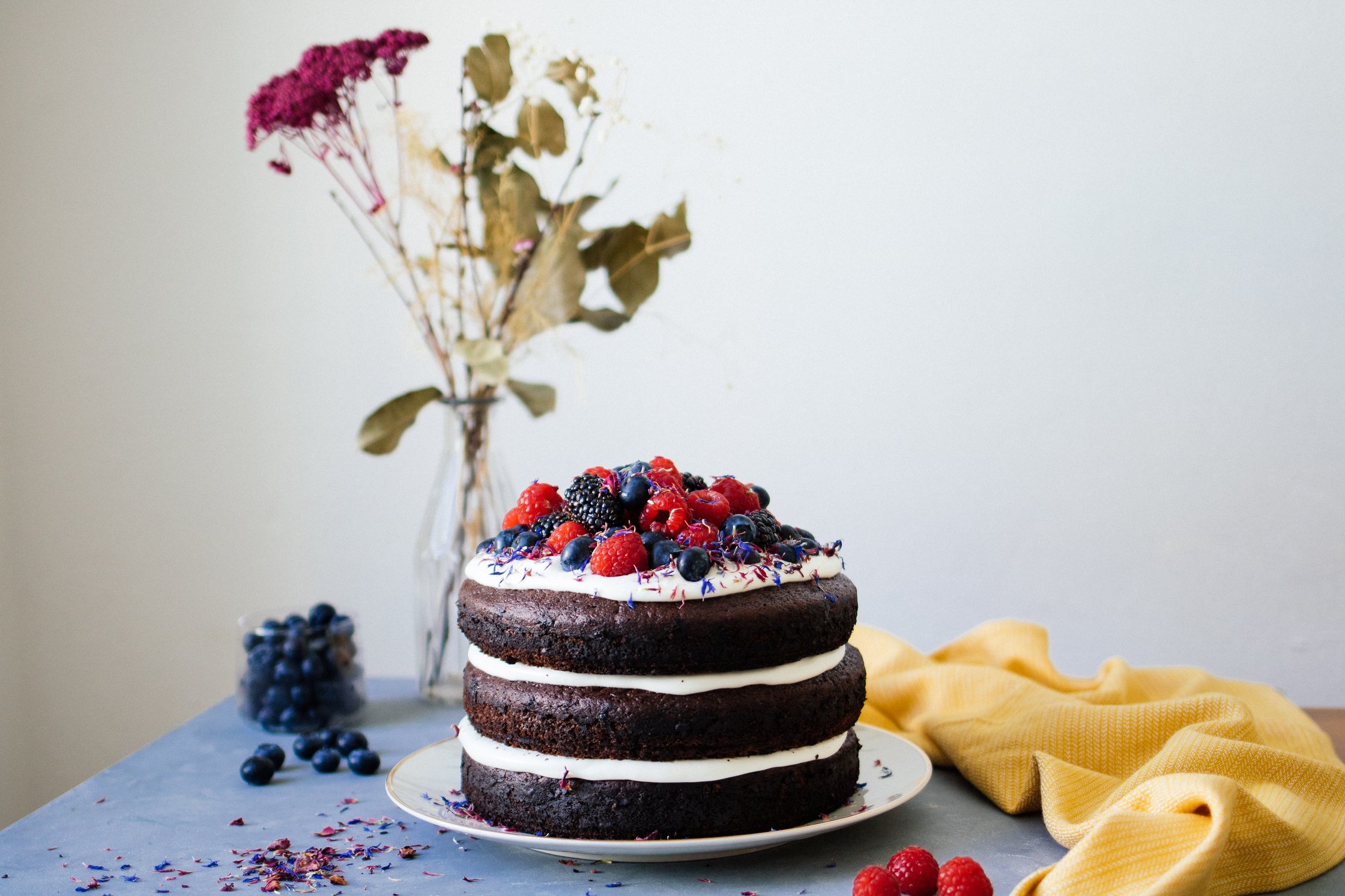 vegane Torte neben Blumen auf einem blauen Untergrund