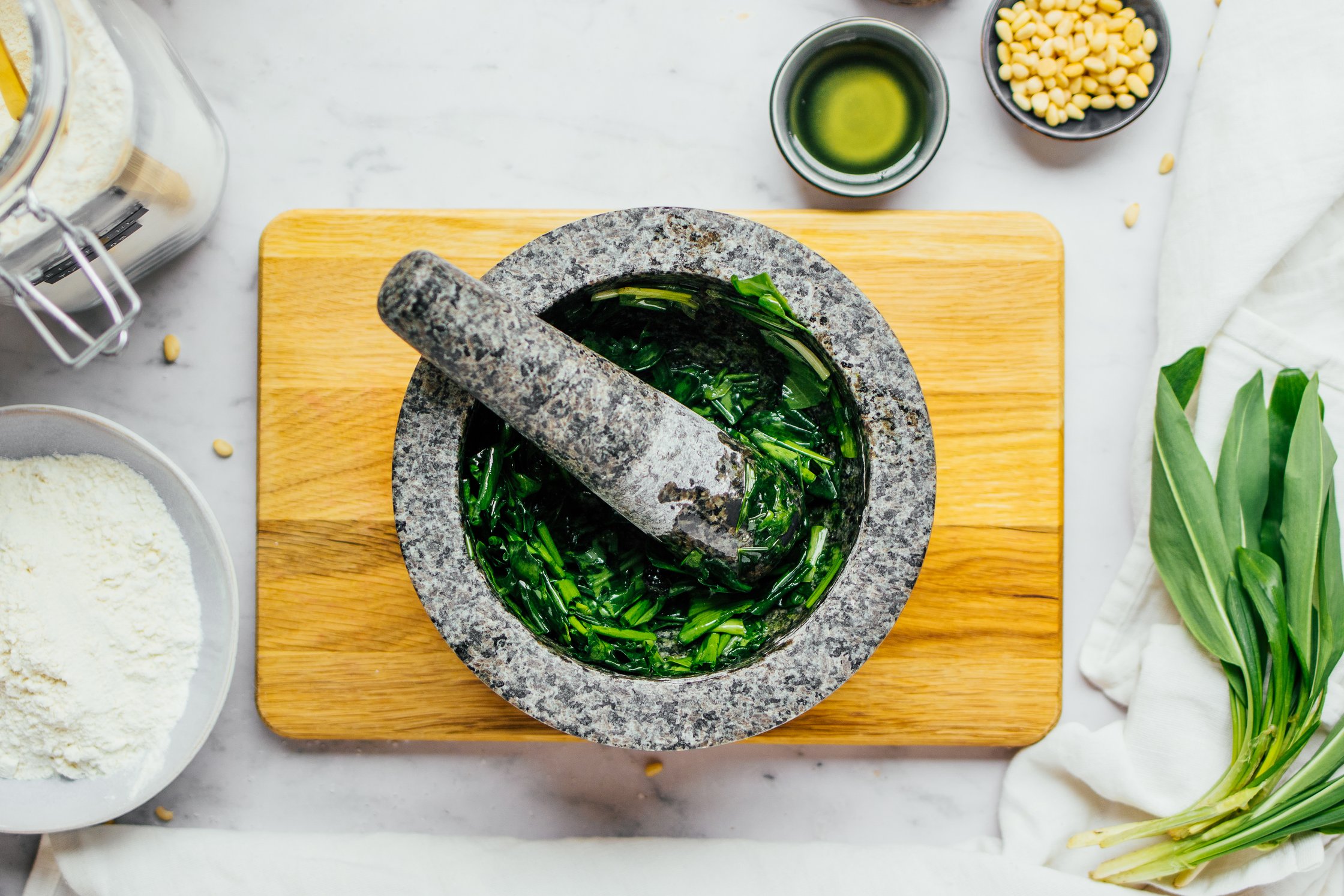 Morter on cutting board with meshed freshly chopped wild garlic and olive oil pesto