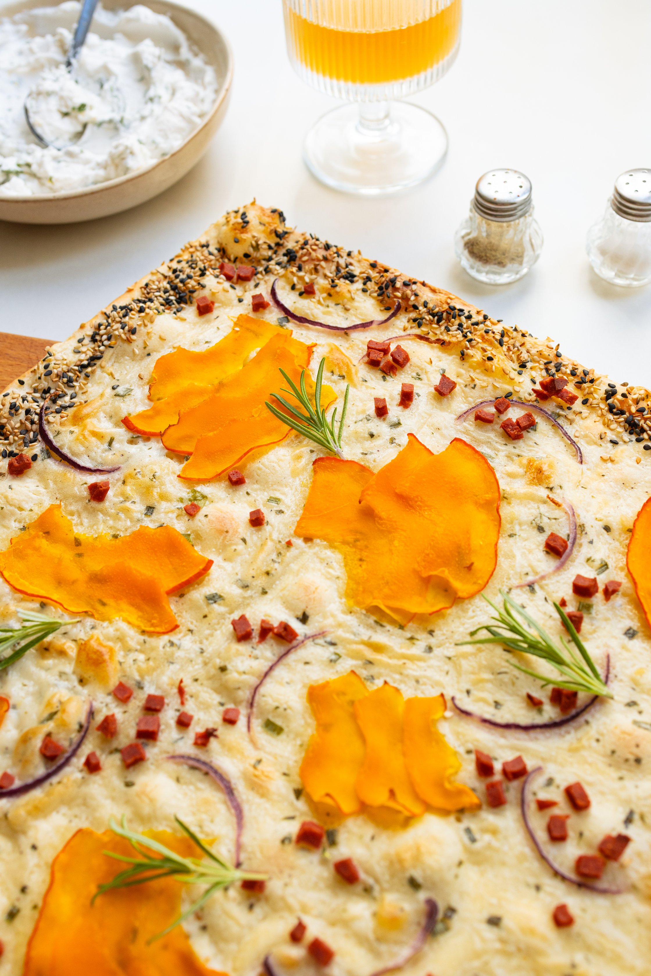 Pumpkin tarte flambée served on a board with a drink and vegan dip.