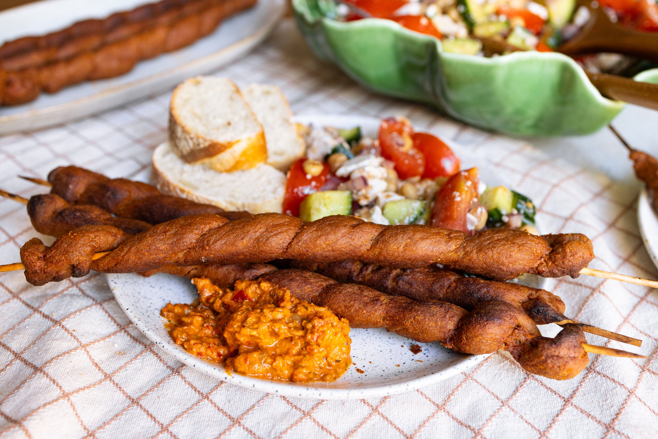 Vegane Grillfackeln mit Baguette, Kichererbsensalat und Tartex Aufstrich auf einem Teller angerichtet.