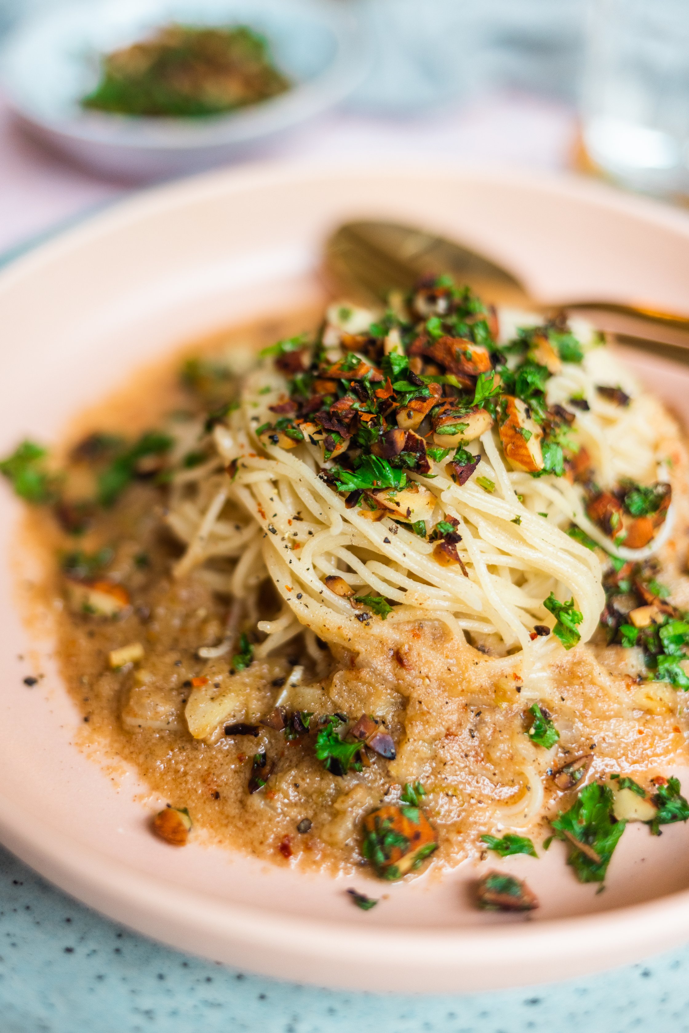 Nahaufnahme von einem Teller Spagghetti in veganer brauner Buttersauce mit Petersilien-Mandel-Topping