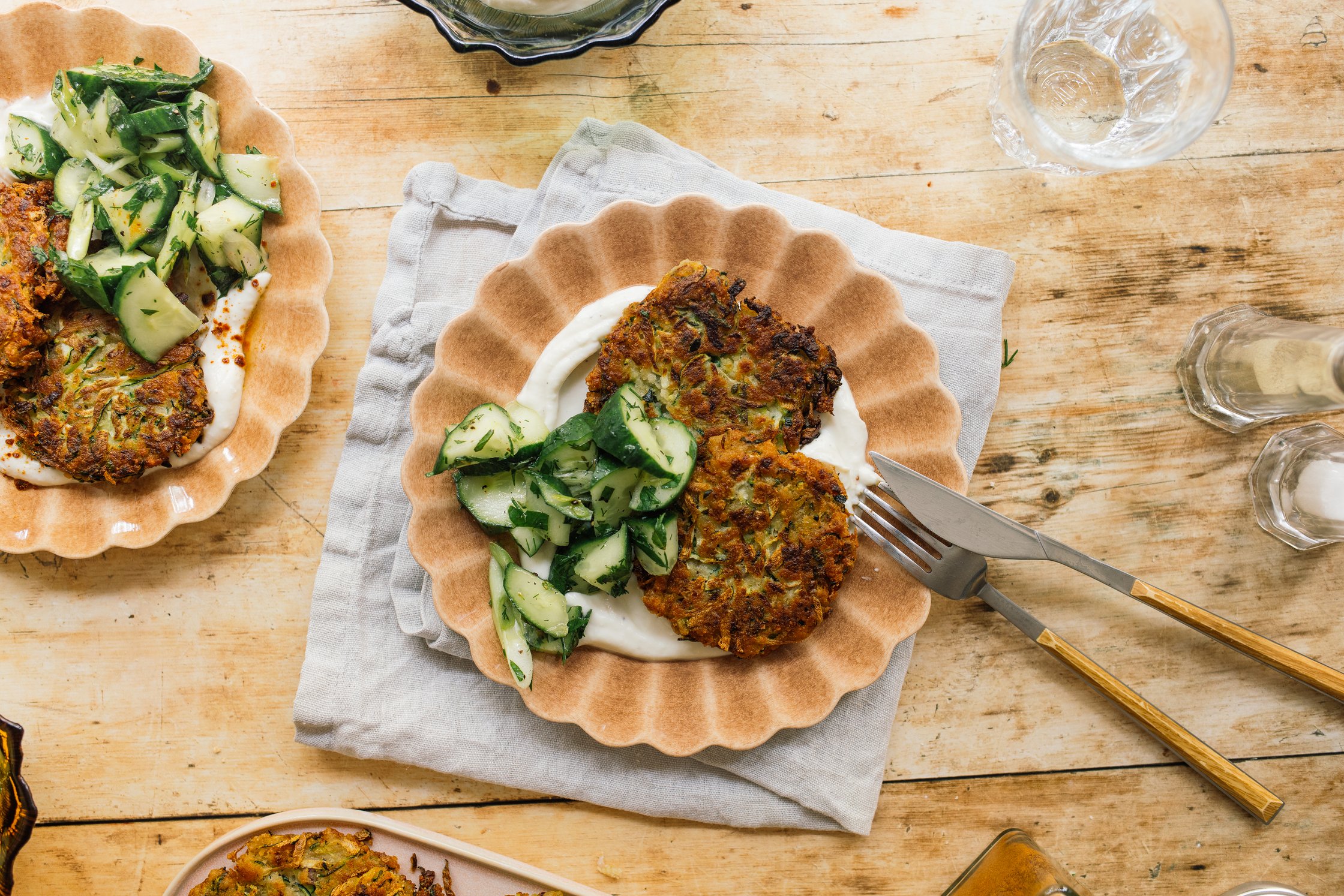 vegane Zucchini-Puffer mit Whipped Feta Dip und Gurkensalat auf einem braunen Teller