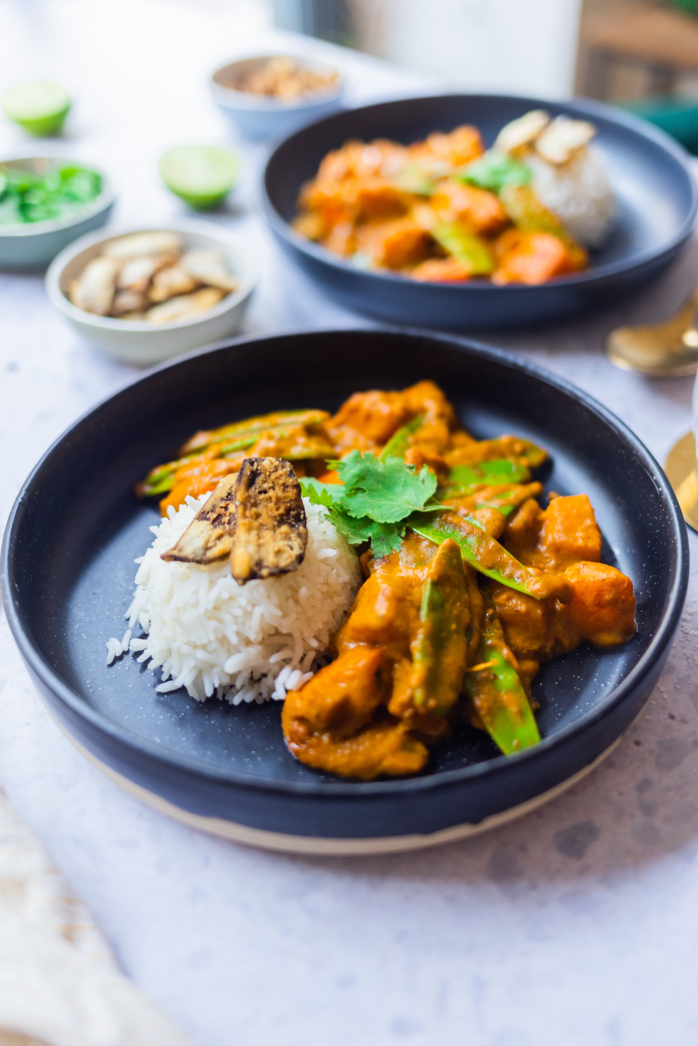 Vegan pumpkin curry is served with ginger chips and coriander on a laid table