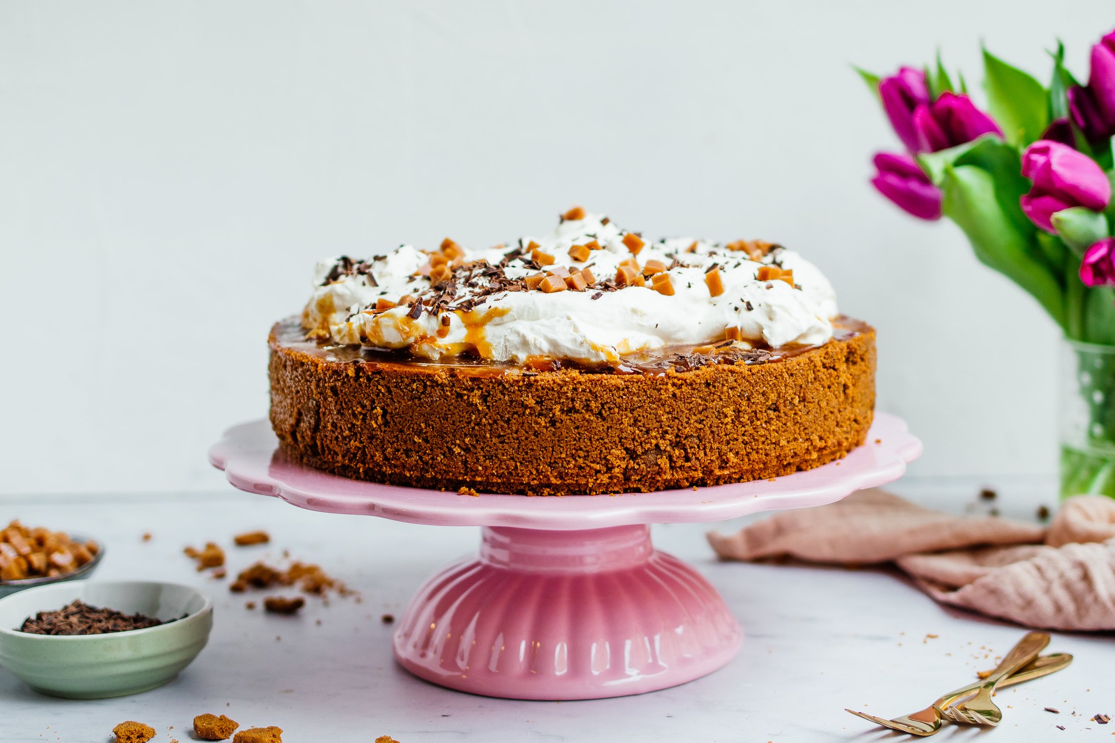 Vegan banoffee pie on a plate with a caramel topping, vegan whipped cream, toffee bites and chocolate shaves