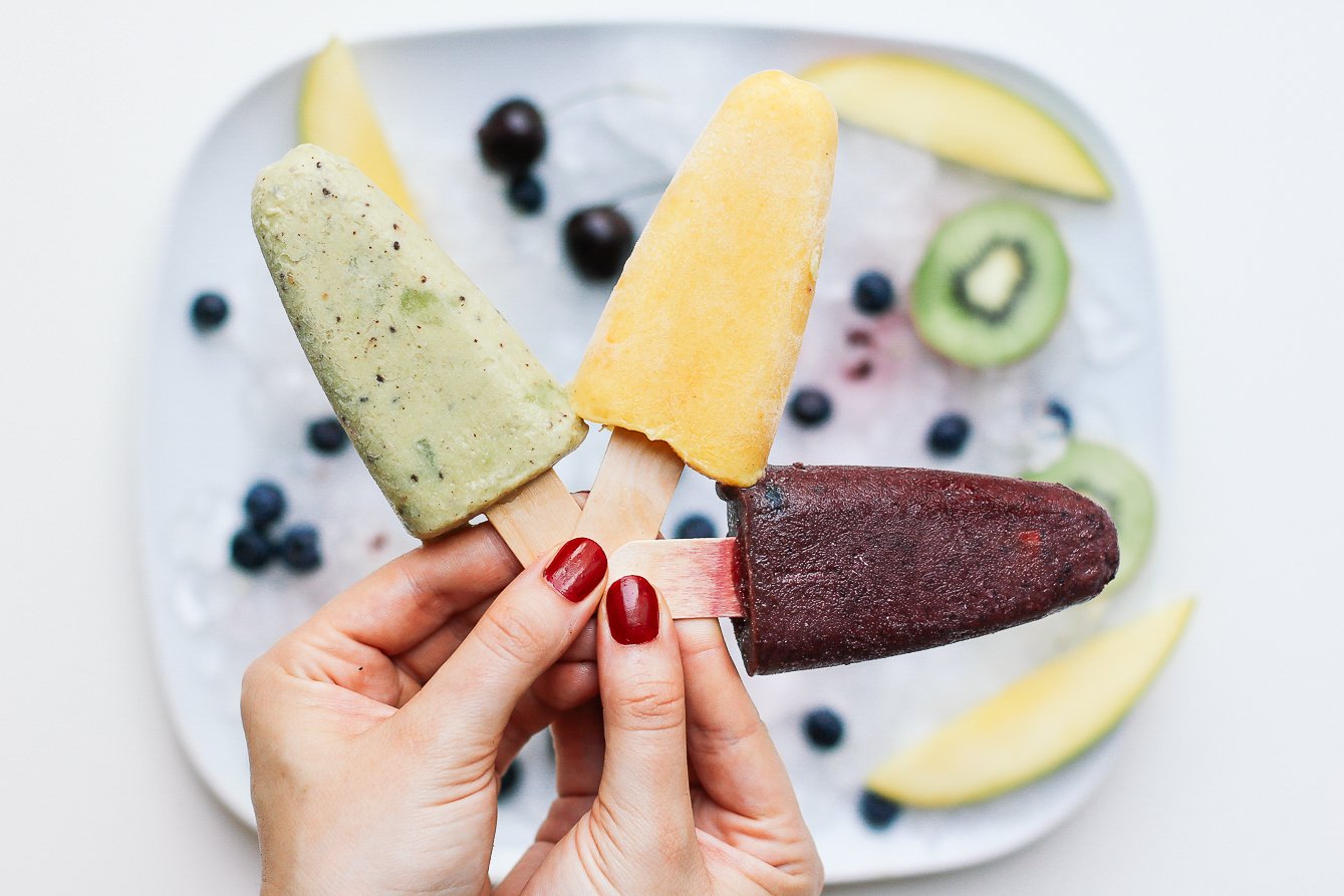 a hand is holding 3 different popsicles