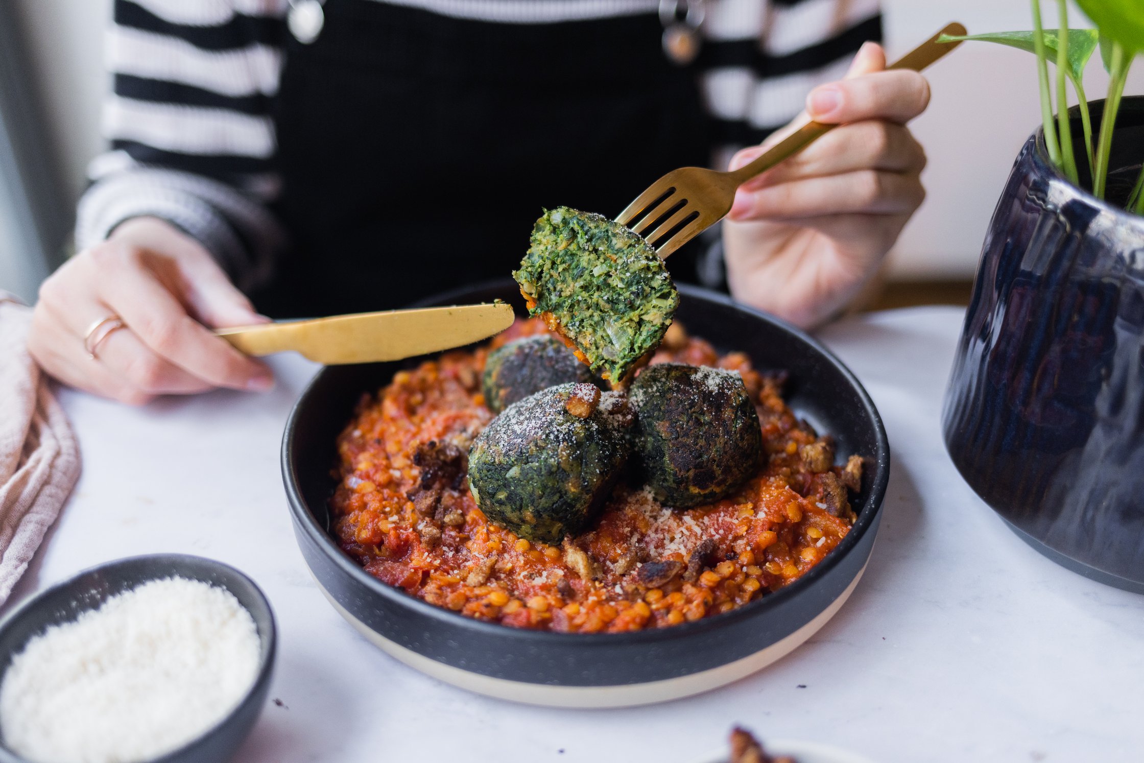 Spinatknödel auf einem Teller mit Tomaten-Linsen-Soße, veganer Parmesan steht daneben