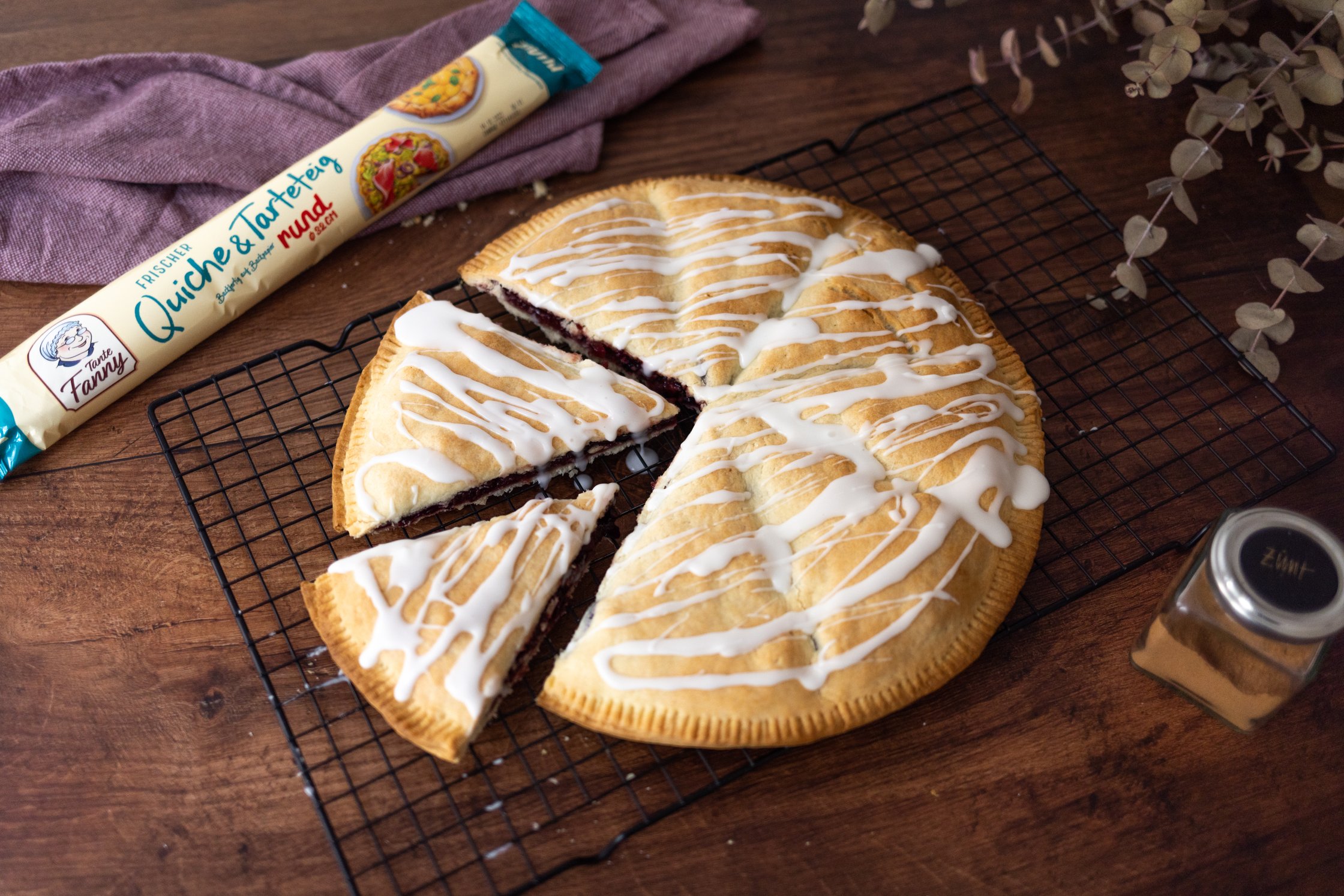 fertig gebackener Apfel Kirsch Hand Pie auf einem Gitter, daneben liegt ein Quiche- und tarteteig und ein küchentuch