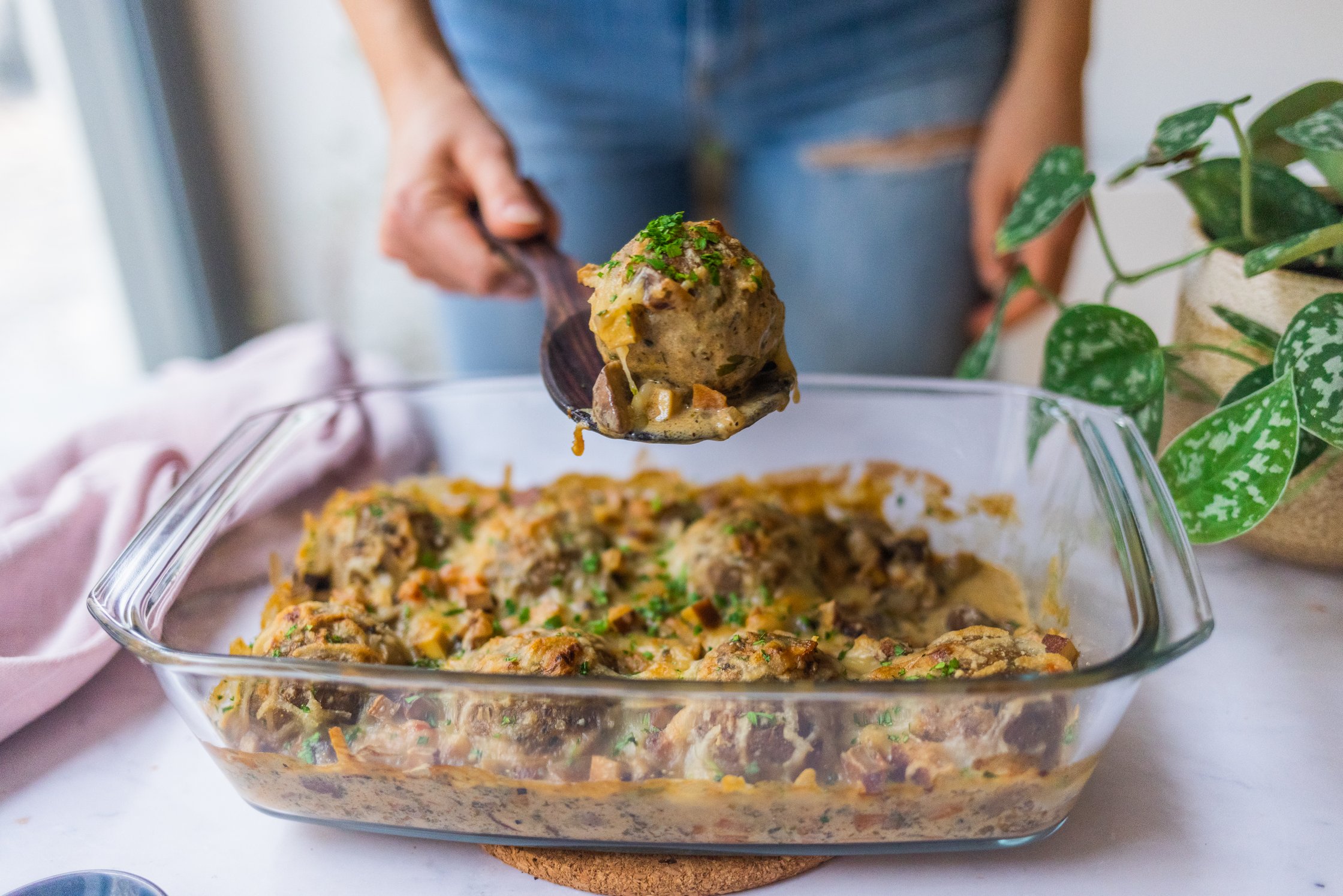 Ein Knödel wird mit einem Holzlöffel aus einem veganen Semmelknödel-Auflauf gehoben.