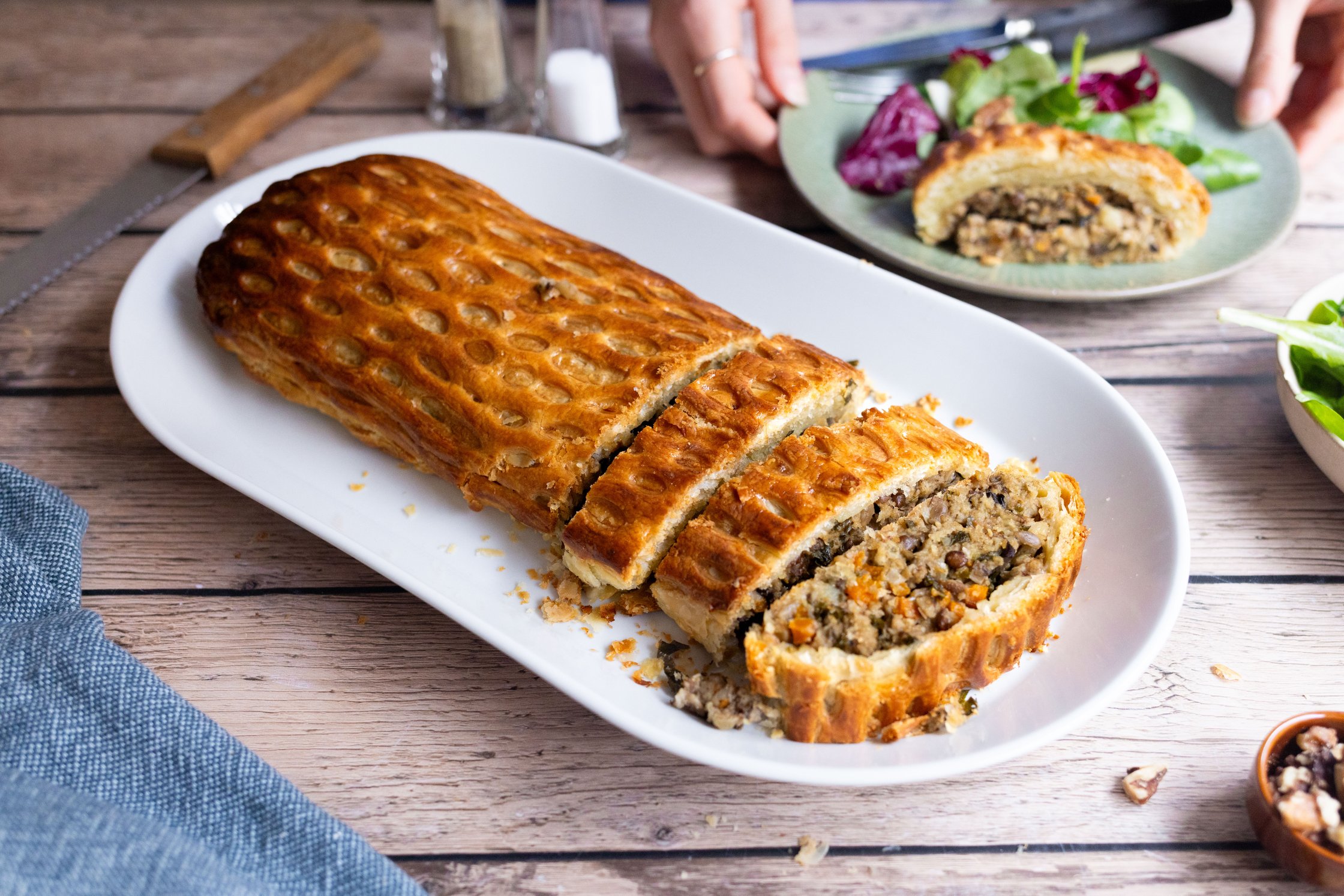 Beef Wellington auf einer Platte, im Hintergrund angerichtet auf Teller mit Salat