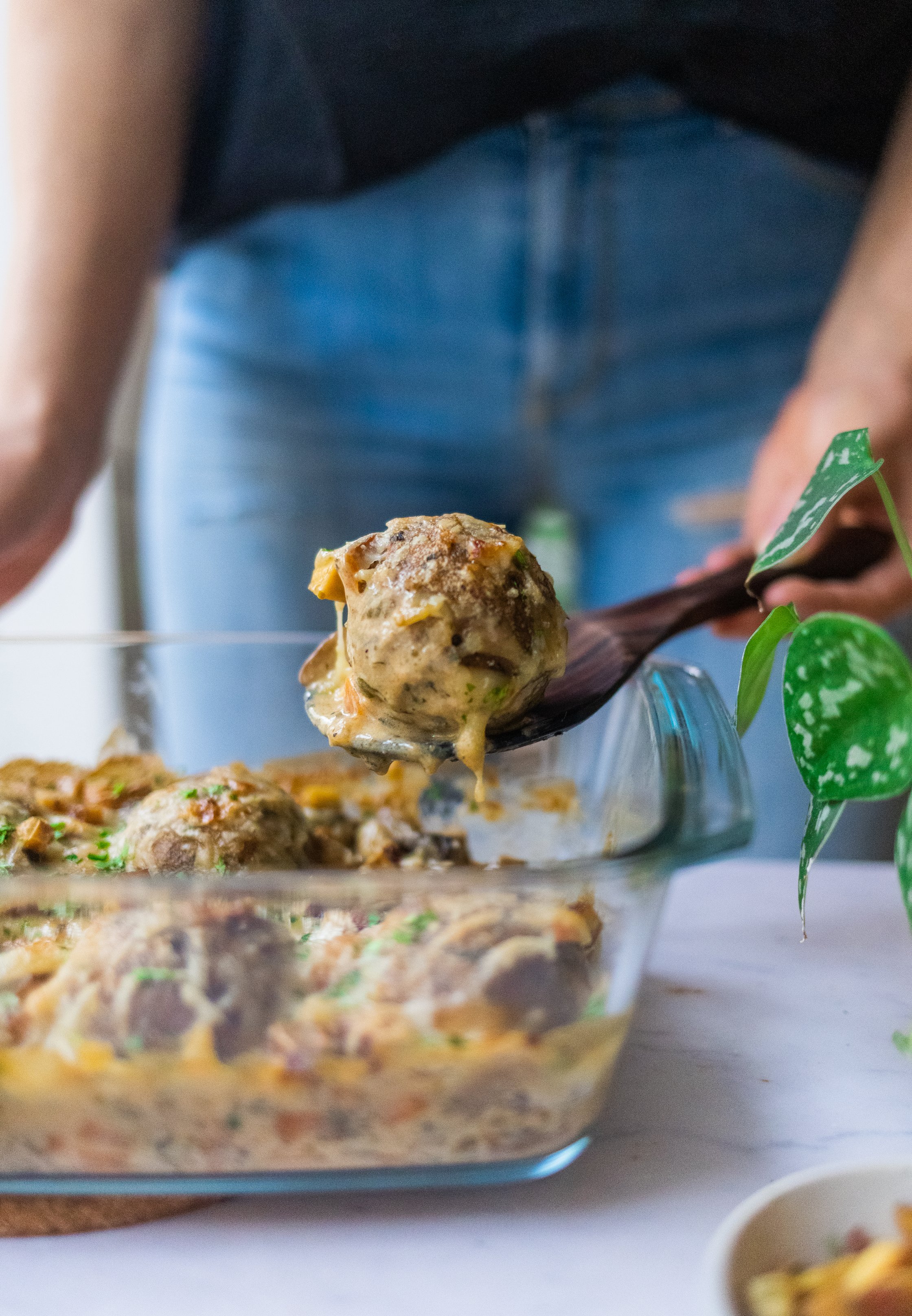 Ein Semmelknödel wird mit einem Holzlöffel aus einem  Semmelknödel-Auflauf genommen und vor die Kamera gehalten.