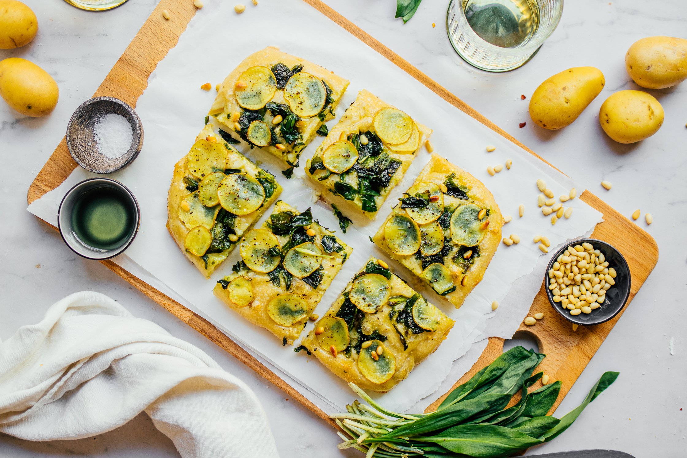 Freshly baked vegan wild garlic focaccia with crispy potato and pine nut topping on wooden board together with fresh ingredie