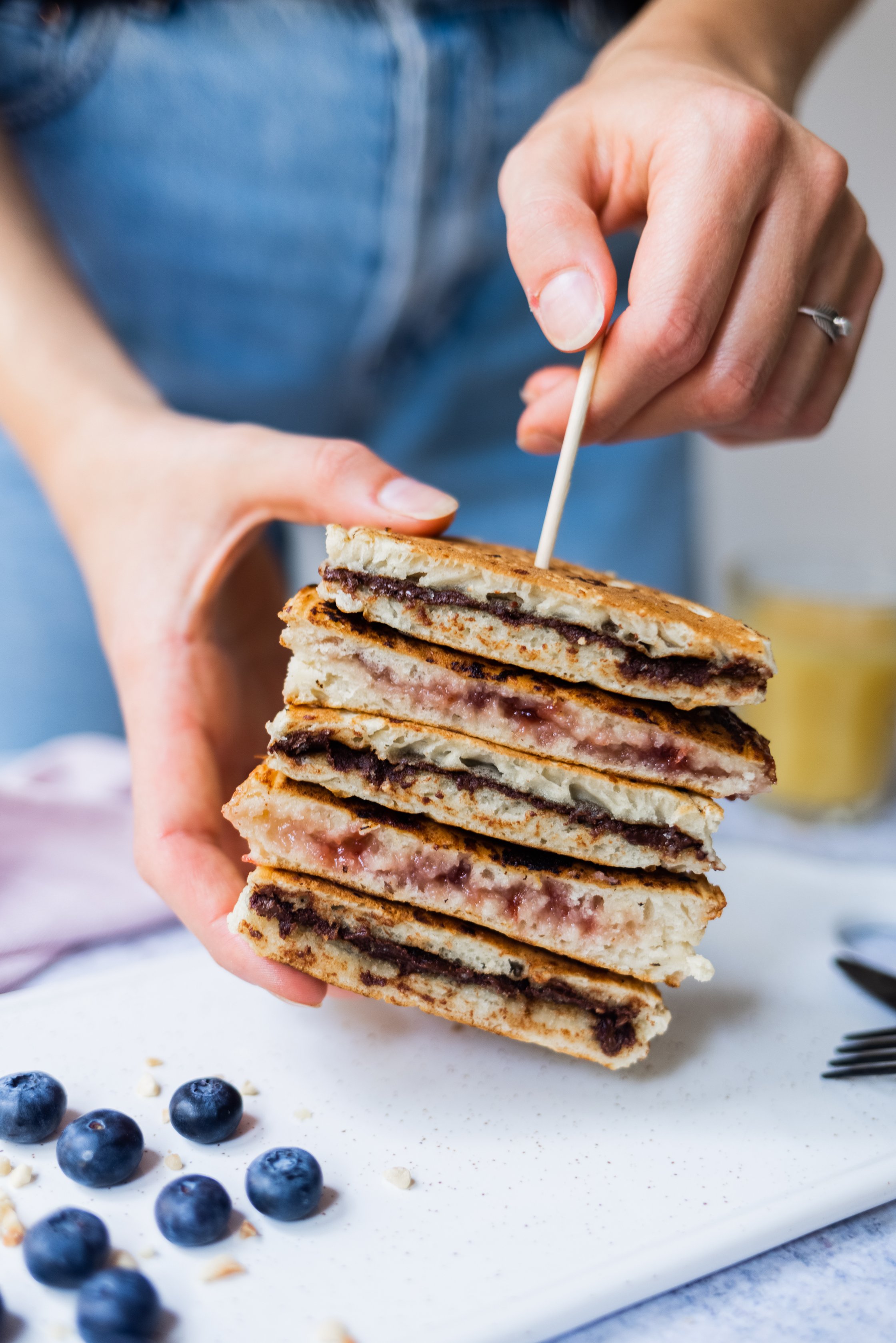 stacked filled pancakes stabilized with a skewer hold with a hand, blueberries