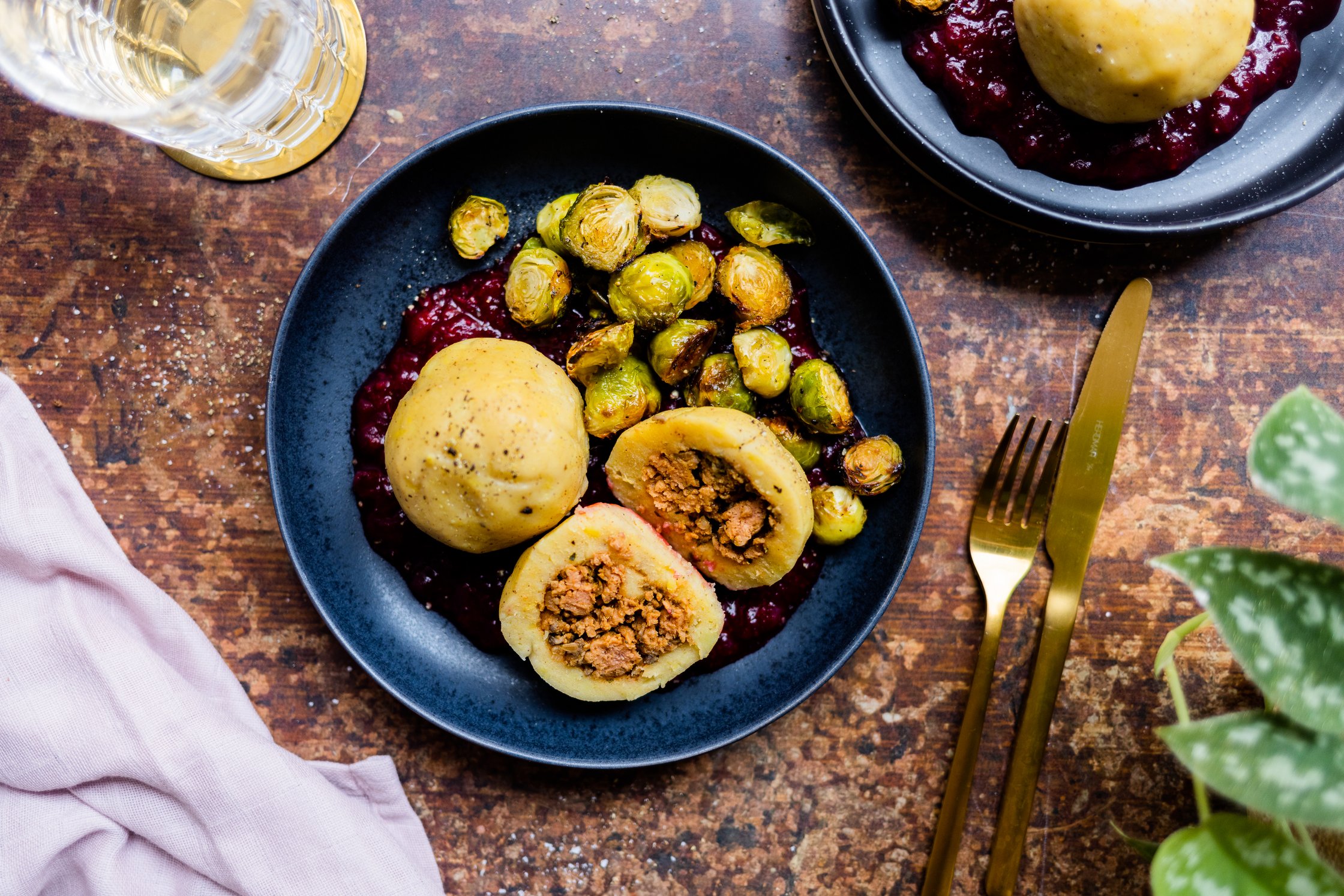 Ein Teller mit gefüllten Knödeln, Rosenkohl und Cranberrysoße, Besteck und Glas stehen daneben