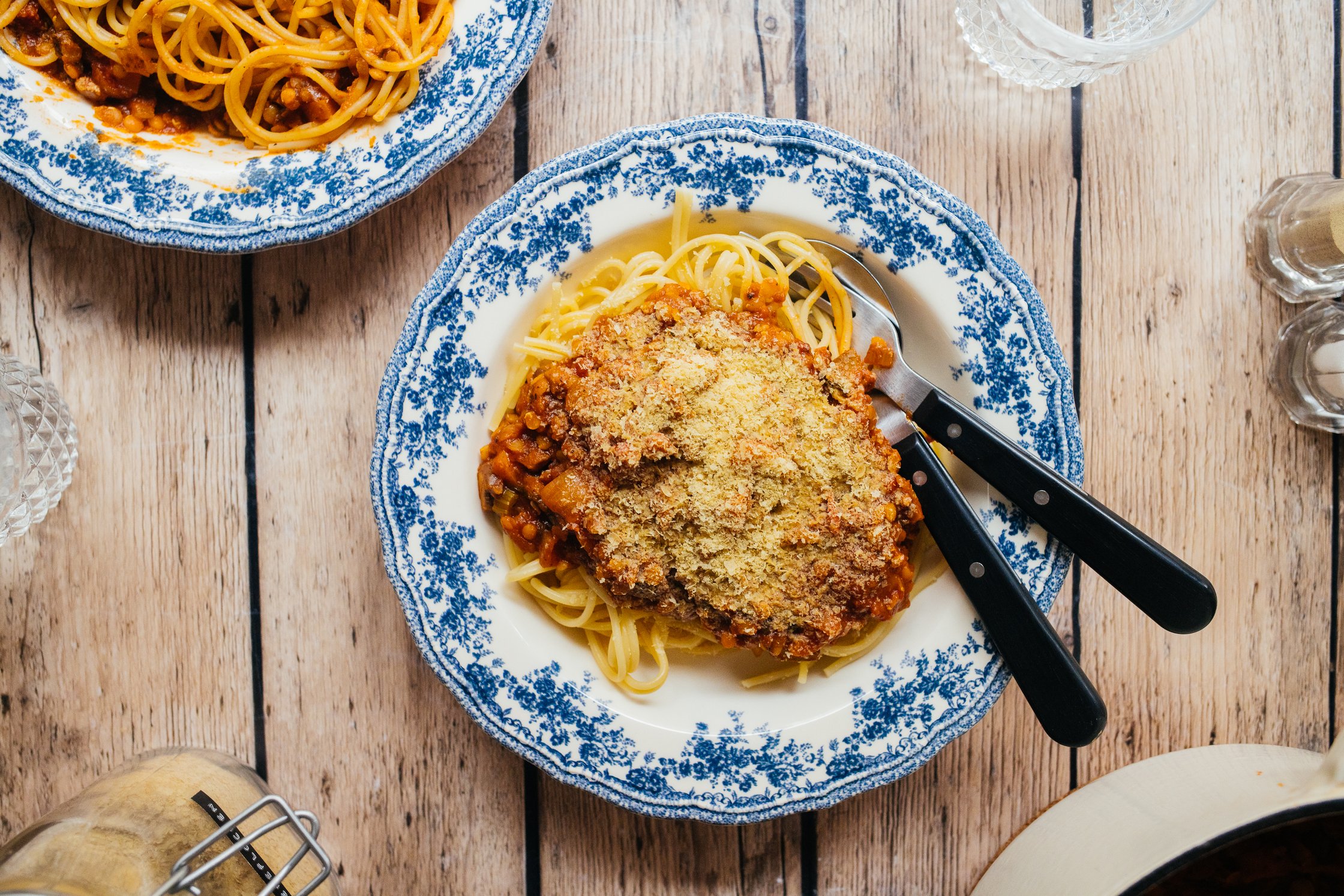 veganer Käse wird auf Linsenbolognese gegeben