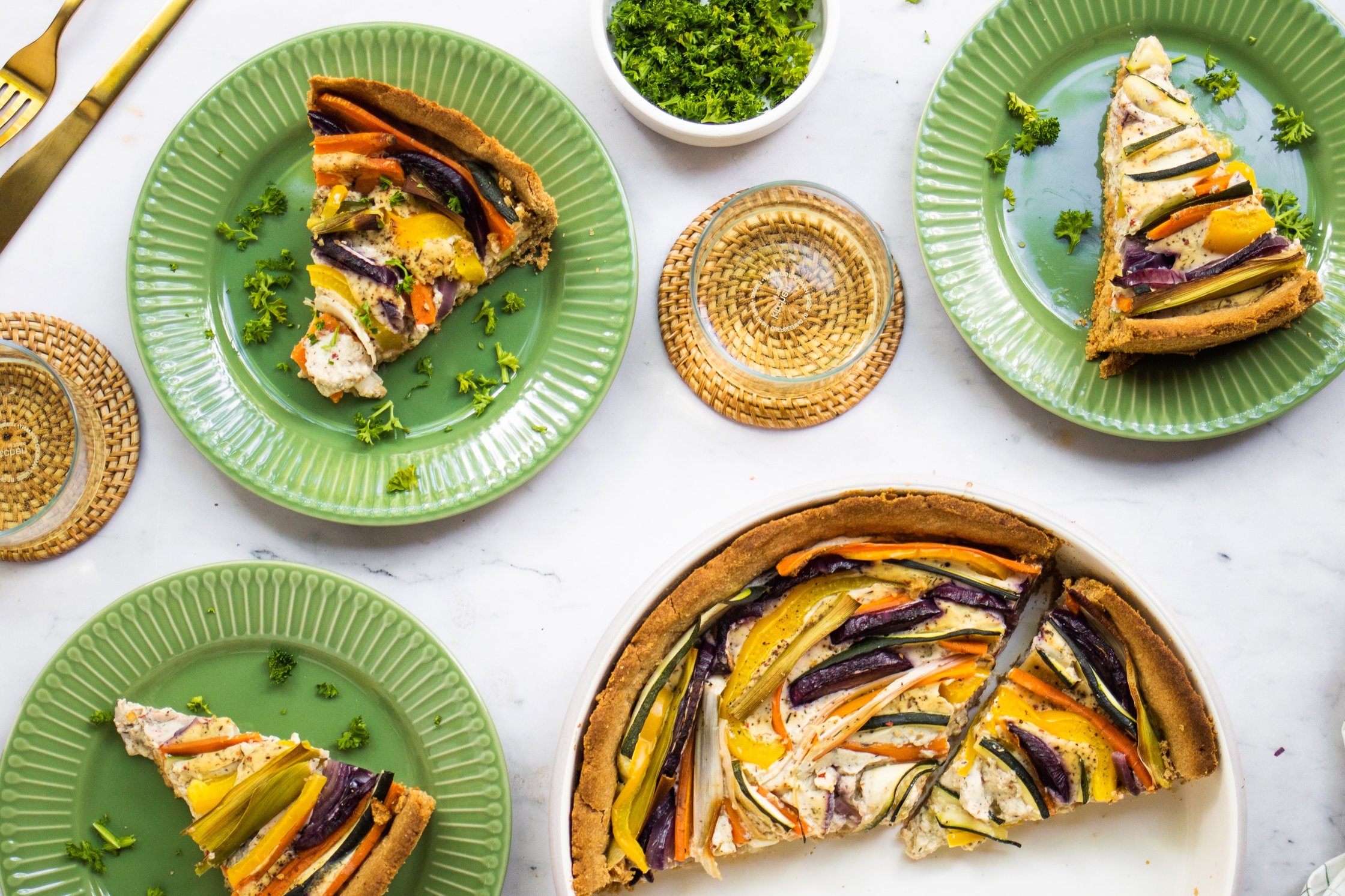 Vegan Vegetable Quiche on plates, glasses of water, fresh parsley, cutlery