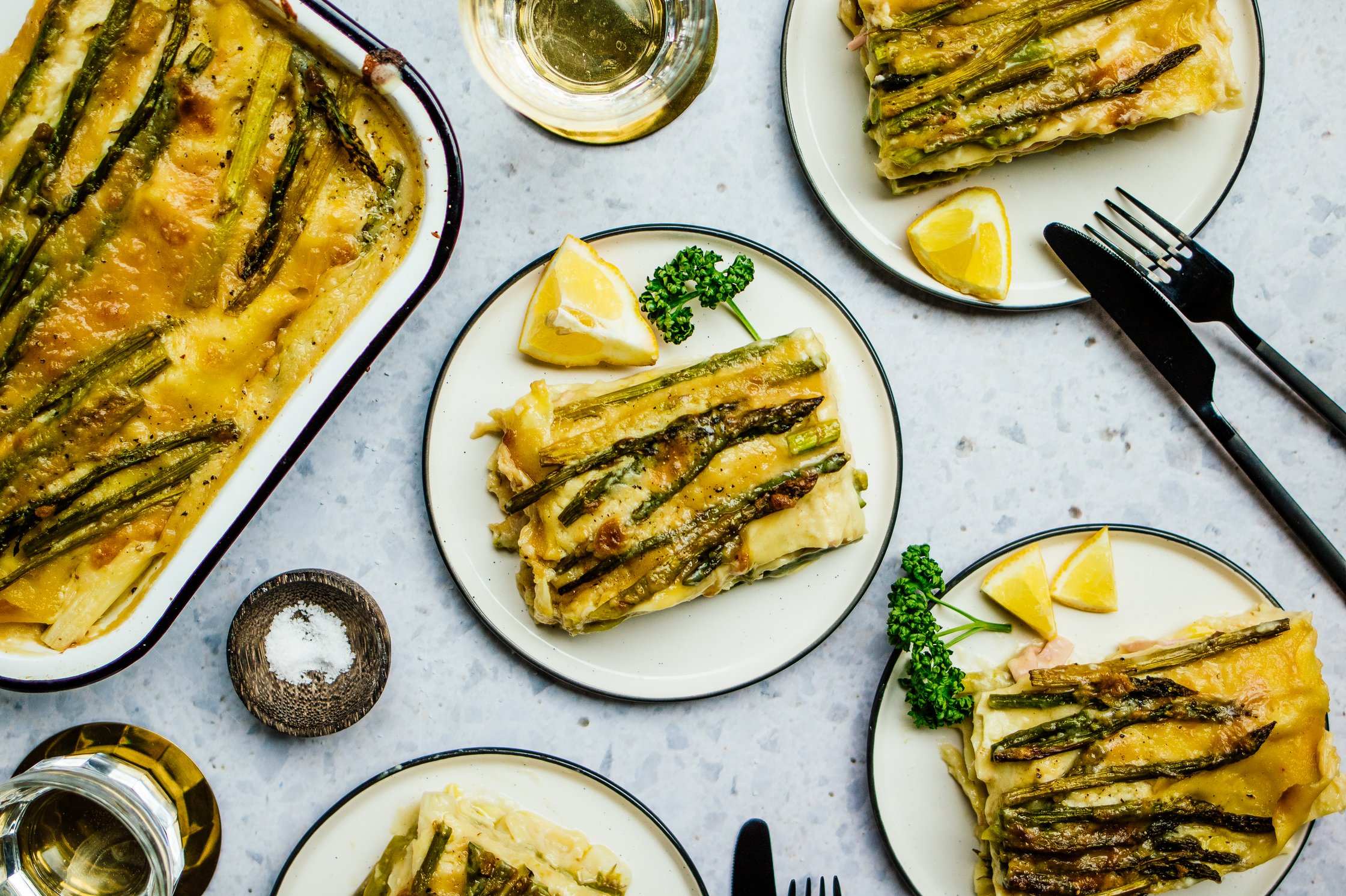 Vegane Spargellasagne verteilt auf vier Tellern mit Zitrone und Petersilie