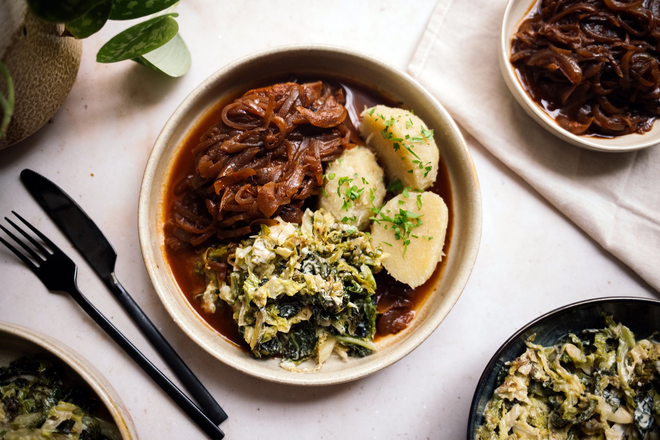 Grüne Klöße mit Zwiebelrostseitan und veganem Rahmwirsing auf einem teller