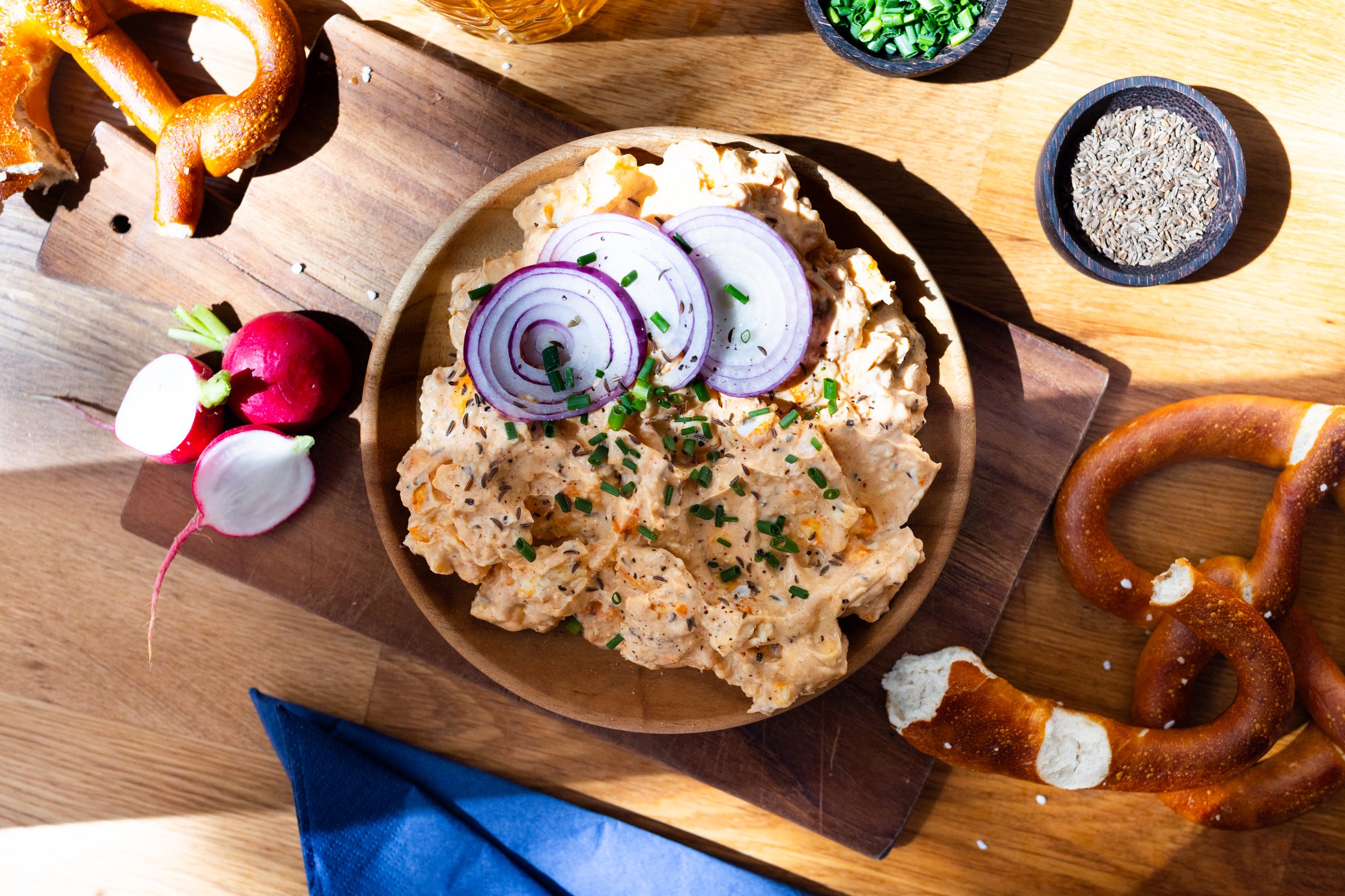 a table set with with vegan Bavarian obazda cheese, red onions, chives, beer and pretzels