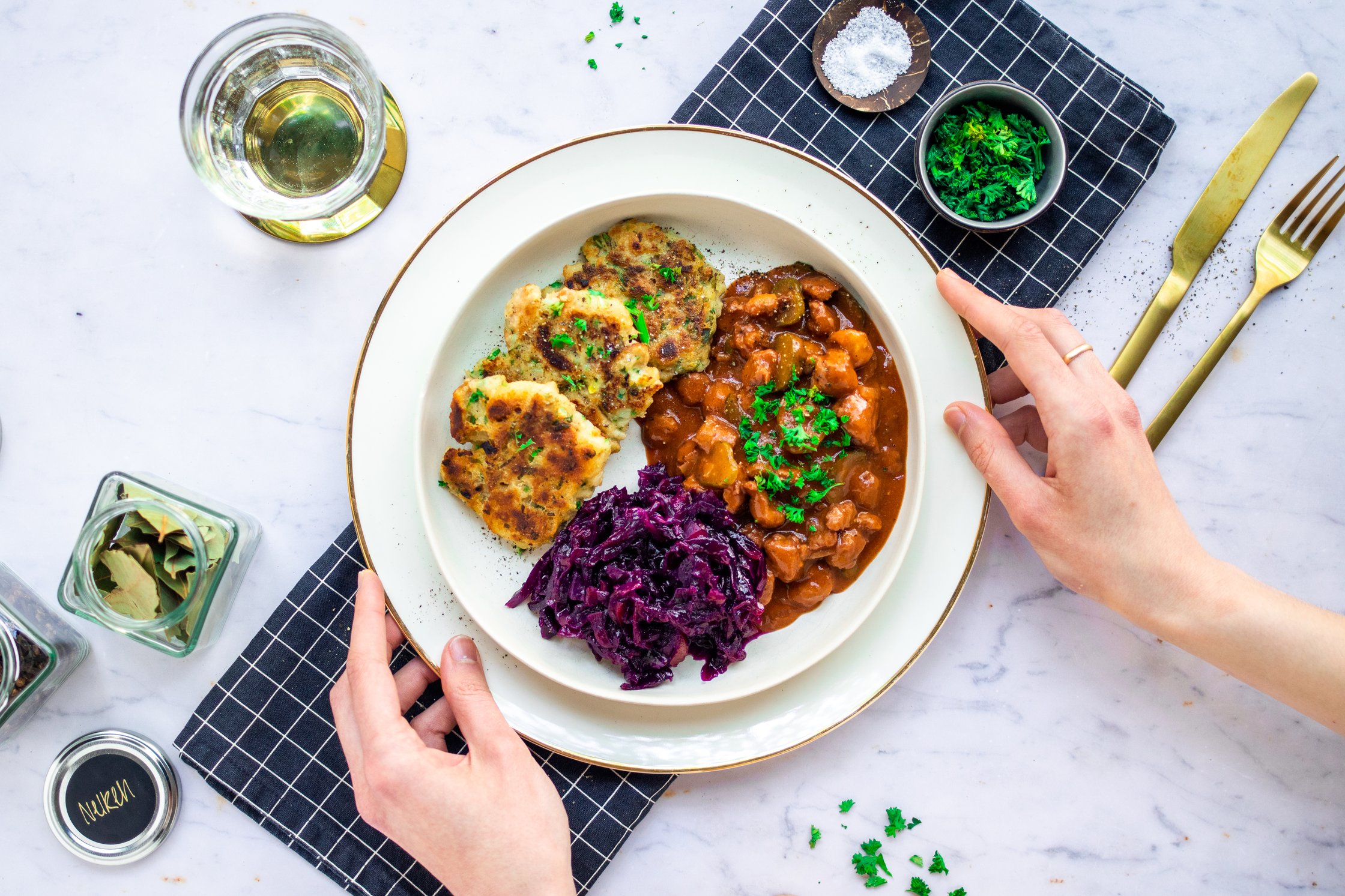 Ein Teller mit Pfannenknödeln, veganem Gulasch und Rotkraut angerichtet auf einem weißen Hintergrund
