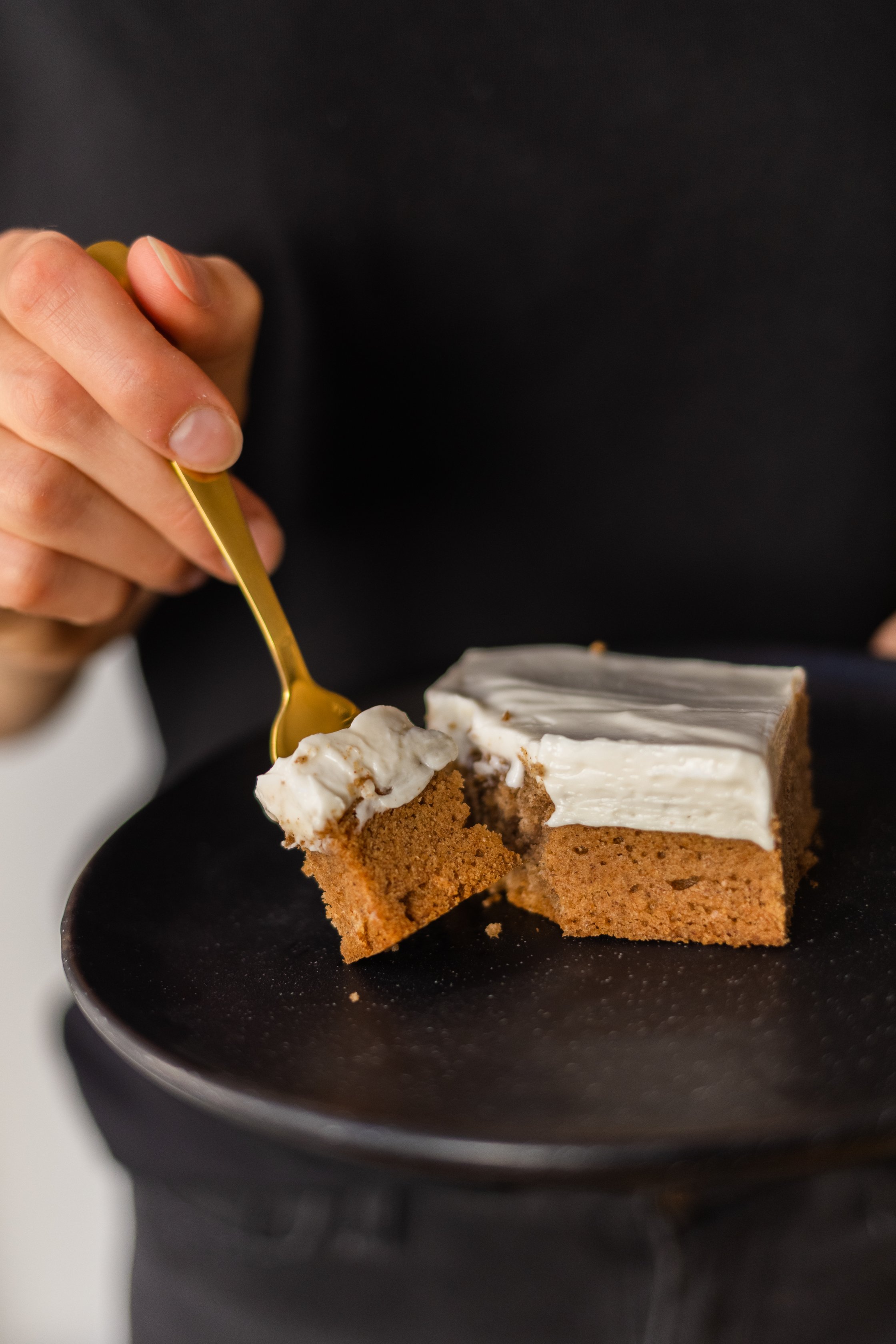 Veganes Gewürzkuchenstück mit Frischkäse-Topping auf einem Teller mit einer Gabel