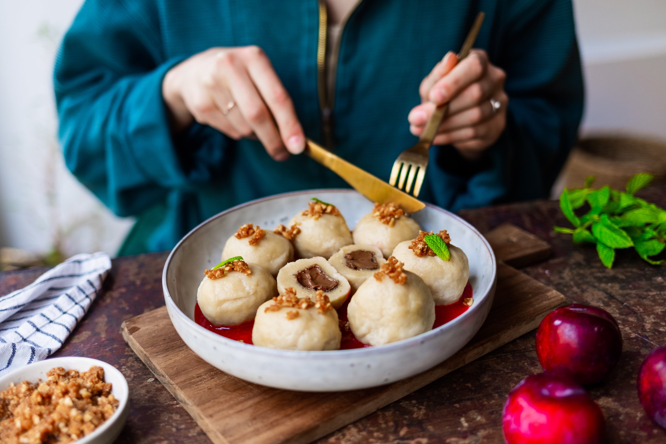 Vegane Nougatknödel mit Zwetschgensoße werden von einem Teller  gegessen.