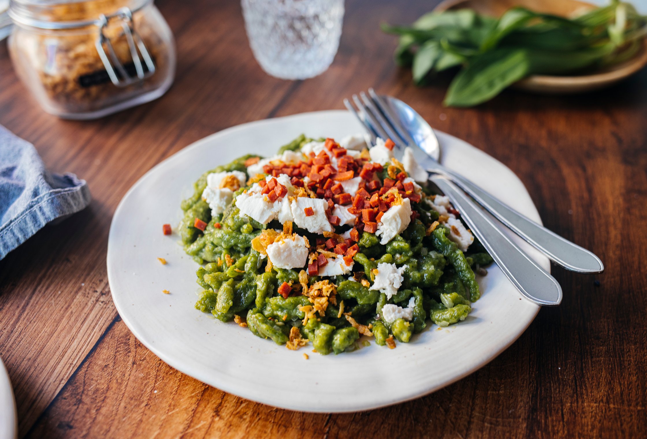 vegan Wild Garlic Spaetzle on a white plate, topped with vegan bacon bits and almond feta cheese