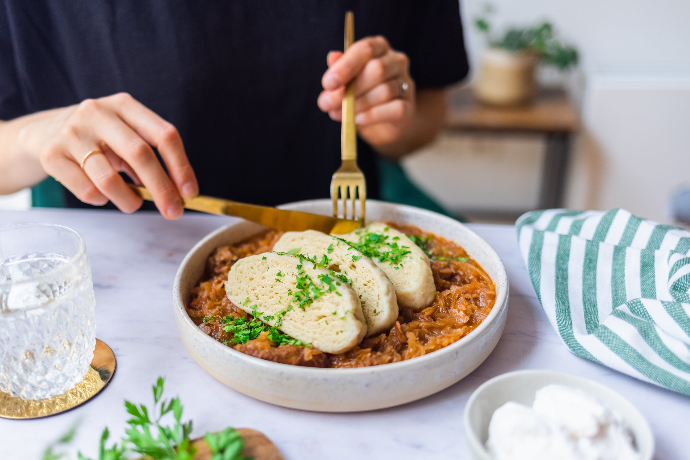 Vegane Böhmische Knödel sind mit Szegediner Gulasch auf einem Teller vor einem hellen Hintergrund angerichtet und werden gege