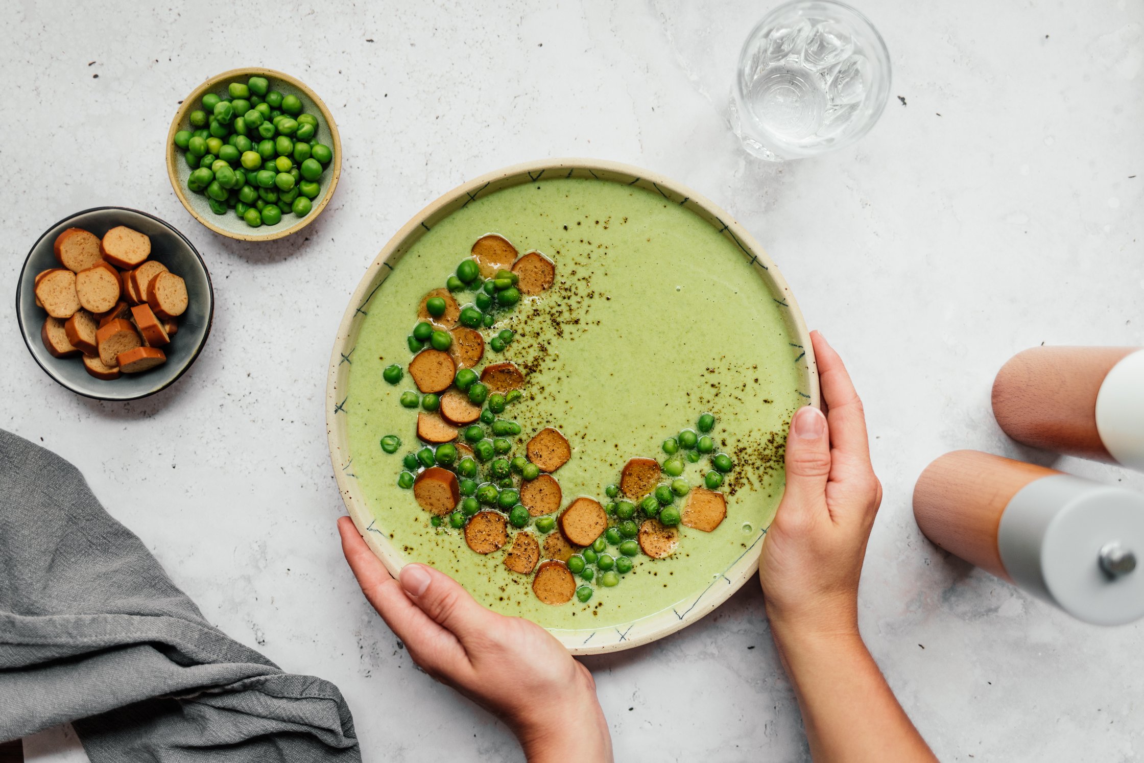 eine Schüssel mit veganer Erbsensuppe mit Würstchen in den Händen