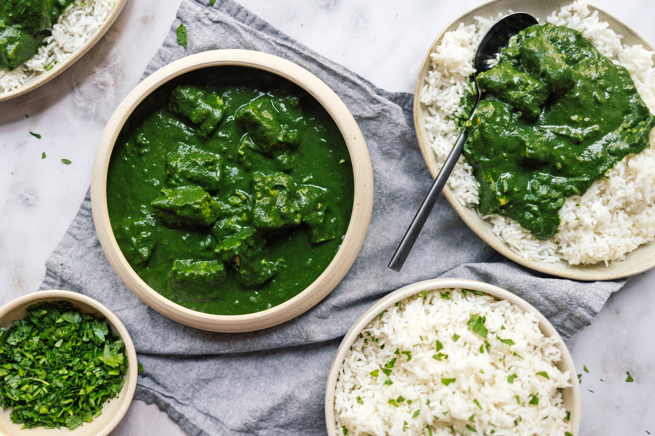 bowls and plates full of rice and vegan palak paneer with tofu