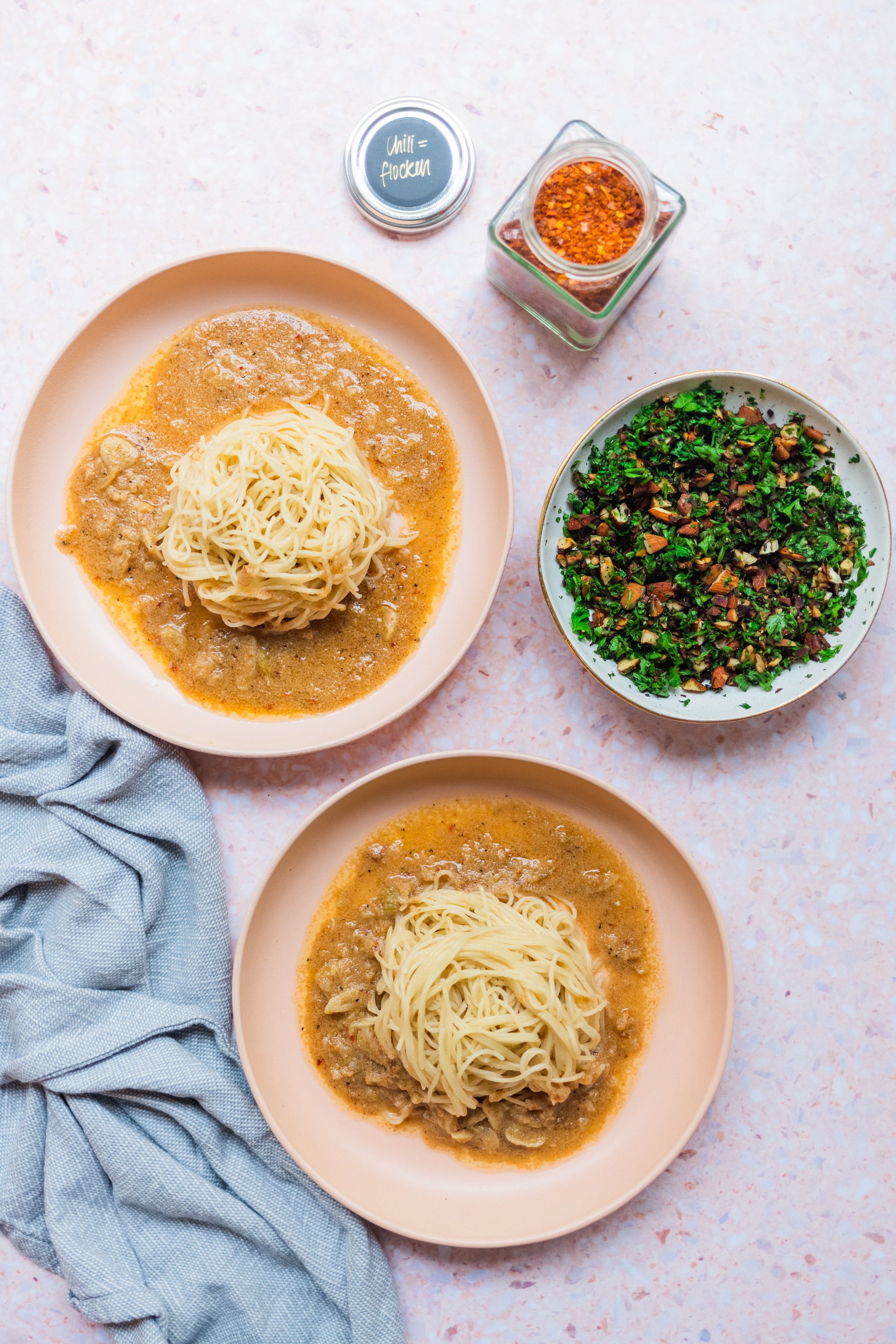 Zwei Teller Spaghetti in veganer brauner Buttersauce vor einem hellen Hintergrund. Daneben eine Schale mit Petersilien-Mandel