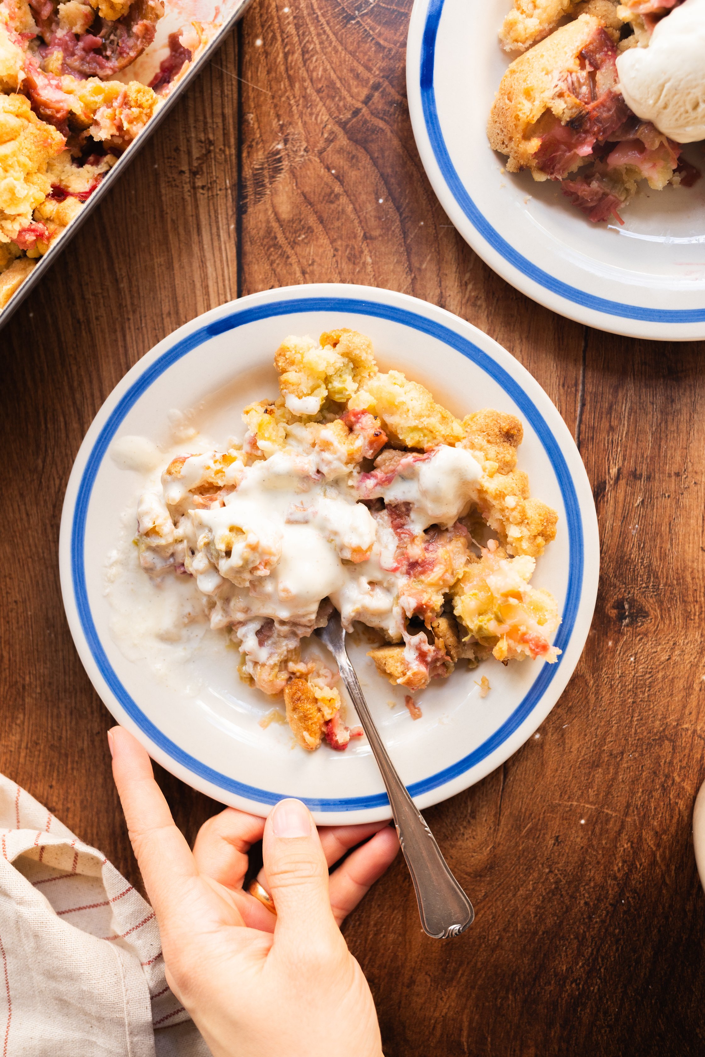 Auf diesem Bild ist eine Hand zu sehen, die einen Teller hält auf dem Der Crumble und Eiscreme vermengt wurde.