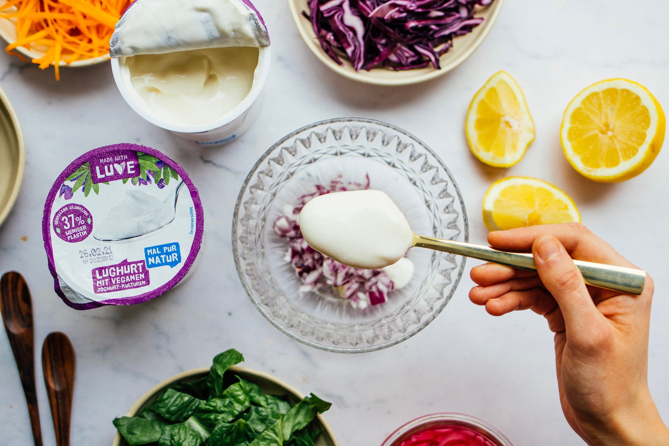 Hand holding spoon wit vegan joghurt over a bowl of red onions