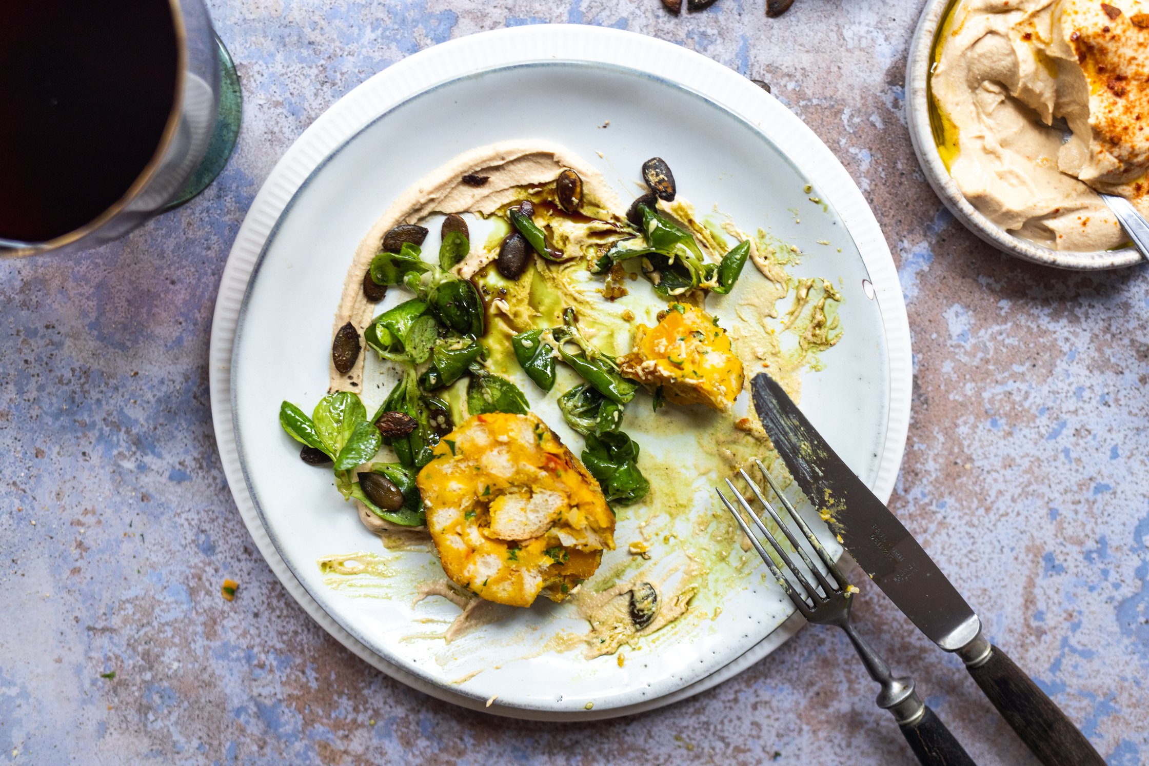 angegessener Teller mit Kürbisknödeln, Feldsalat und Tofu-Creme mit Kürbiskernen