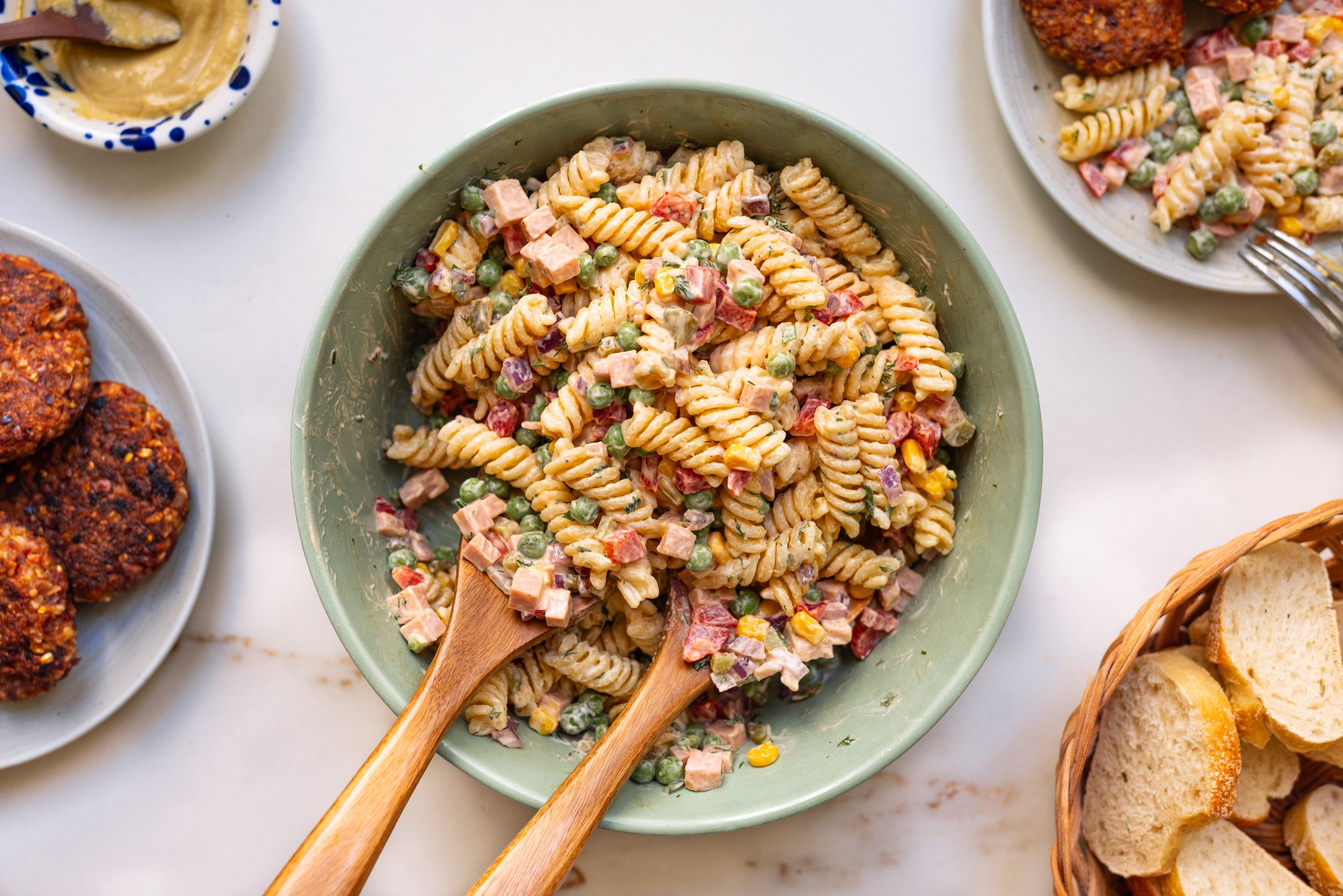 Vegan pasta salad with mayo dressing in a large bowl, served with vegan patties on the side.