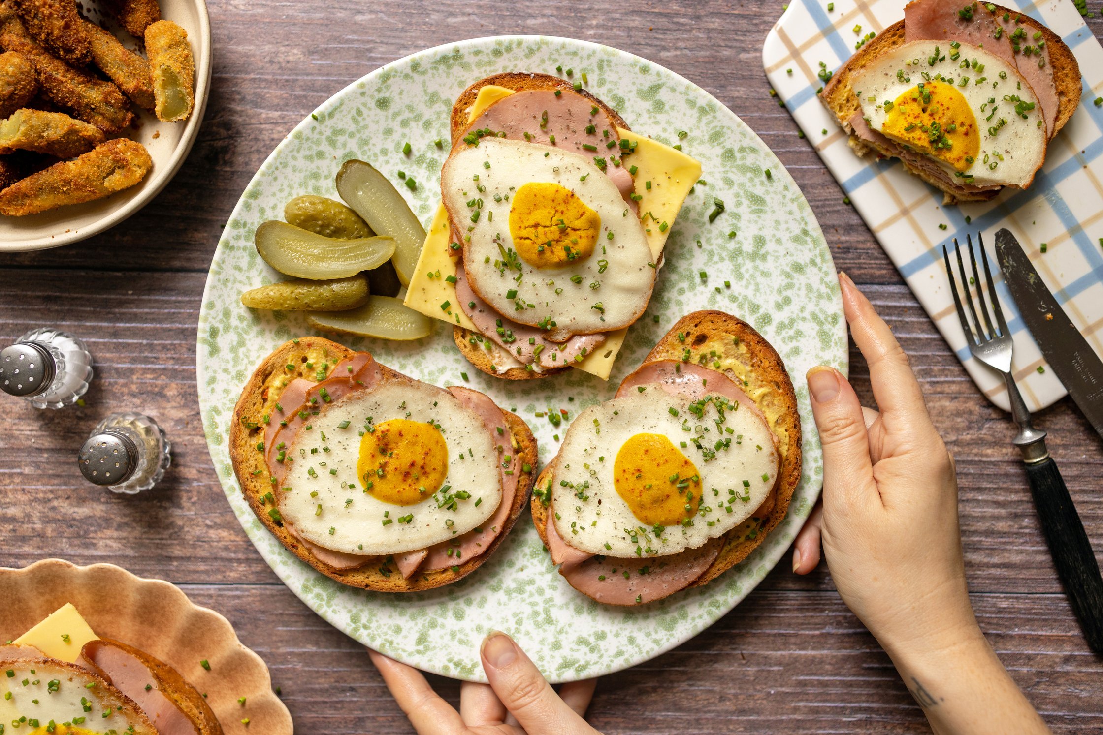 A top-down shot of a large plate with three open-faced sandwiches topped with ham, cheese, and a fried egg.