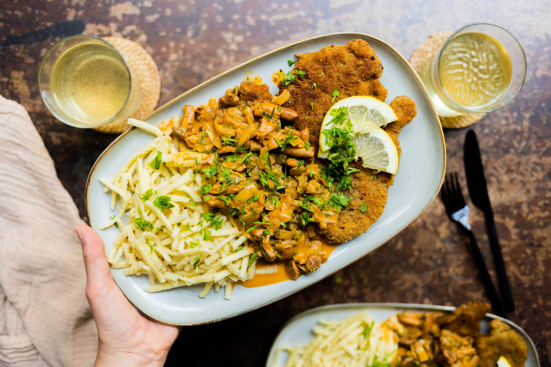 Veganes Jägerschnitzel mit Pfifferlingen und Spätzle auf einem Teller mit Besteck und Gläsern