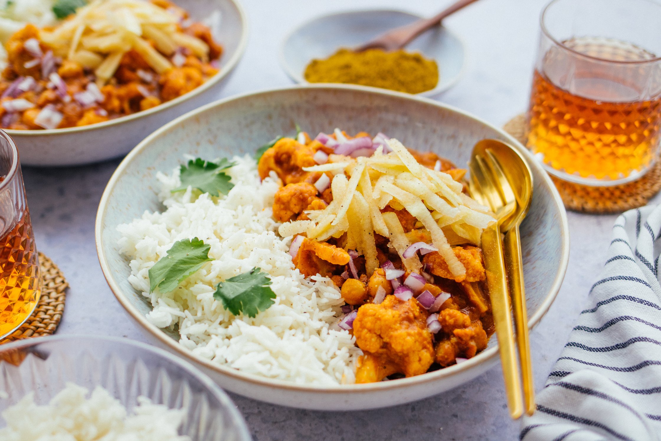 A bowl of vegan chicken madras with rice in the center, also glasses of tea and bowls in the background