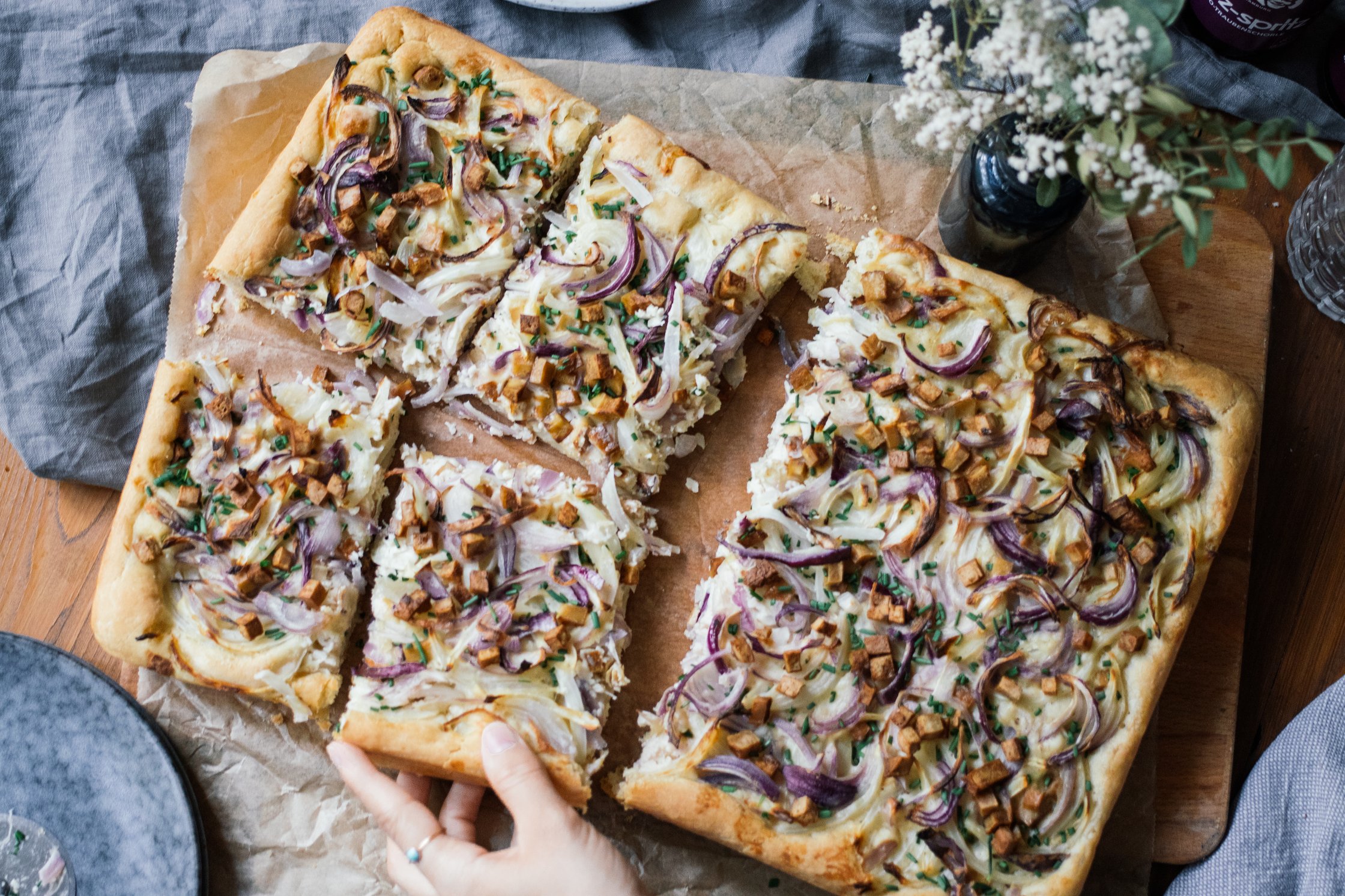 eine hand nimmt sich ein stück vom Veganen Zwiebelkuchen vom Blech
