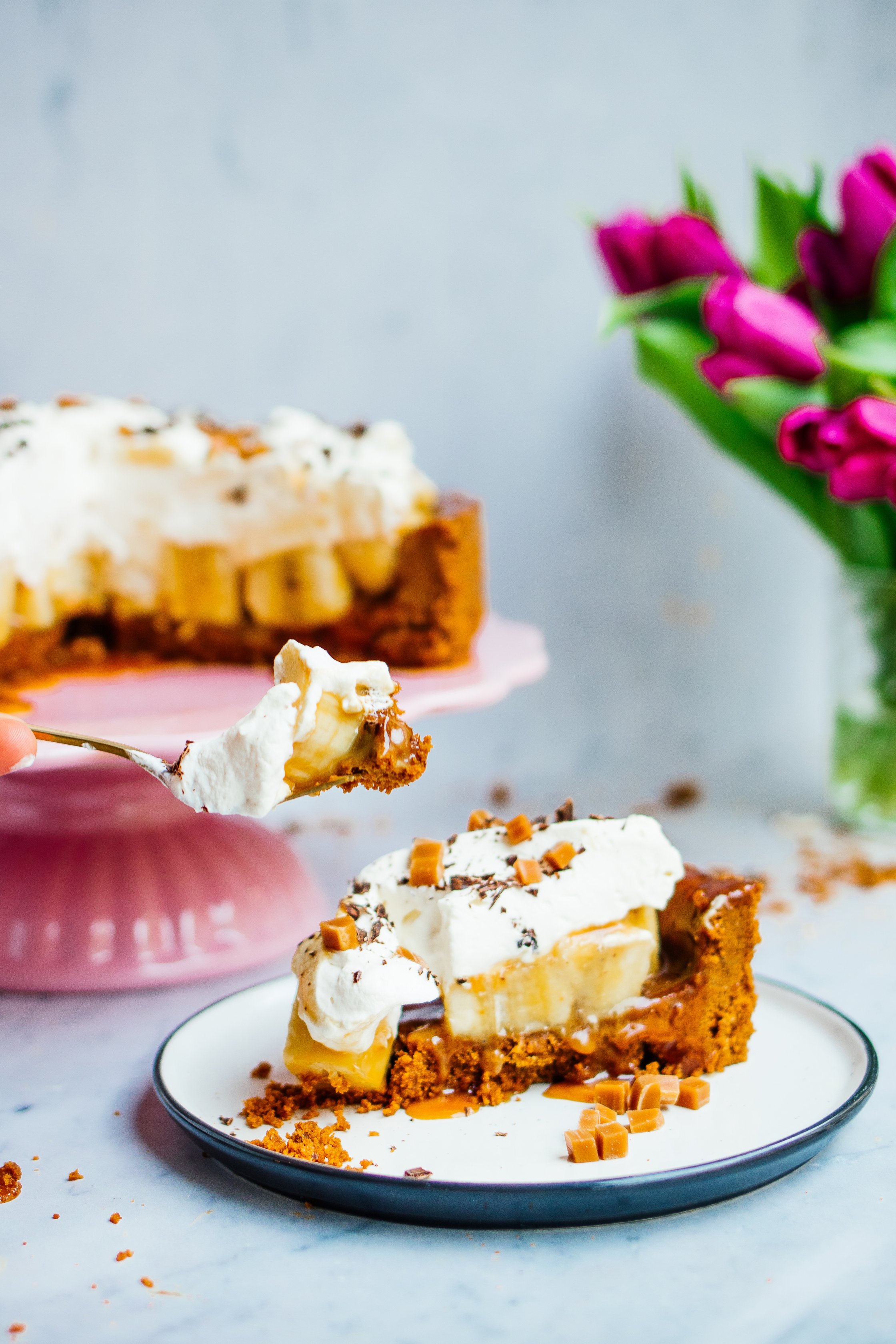 Sliced vegan banoffee pie with vegan whipped cream topping, plate with piece of vegan banoffee pie and fork