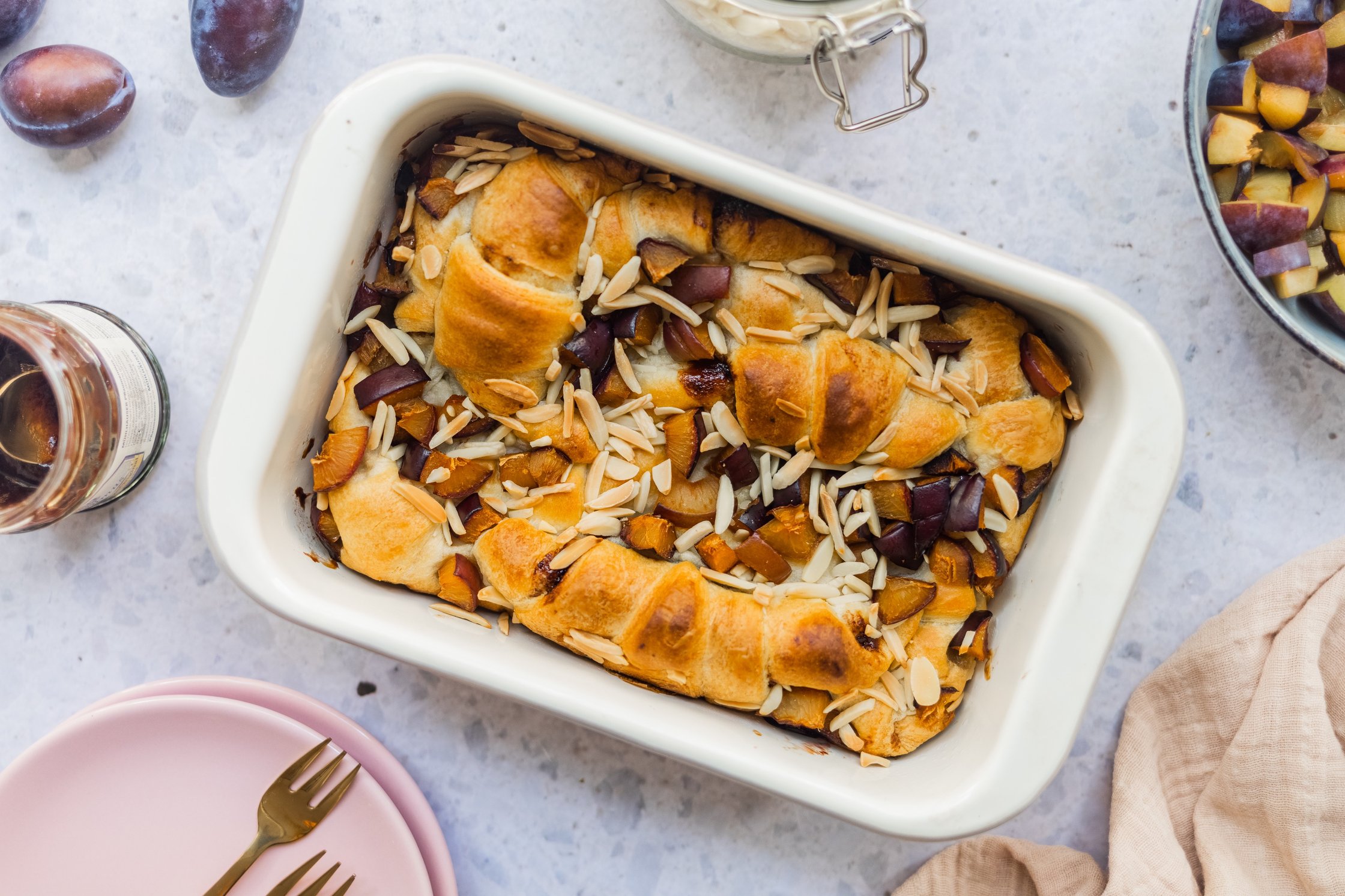 vegan croissant casserole with plums and almonds in a baking dish