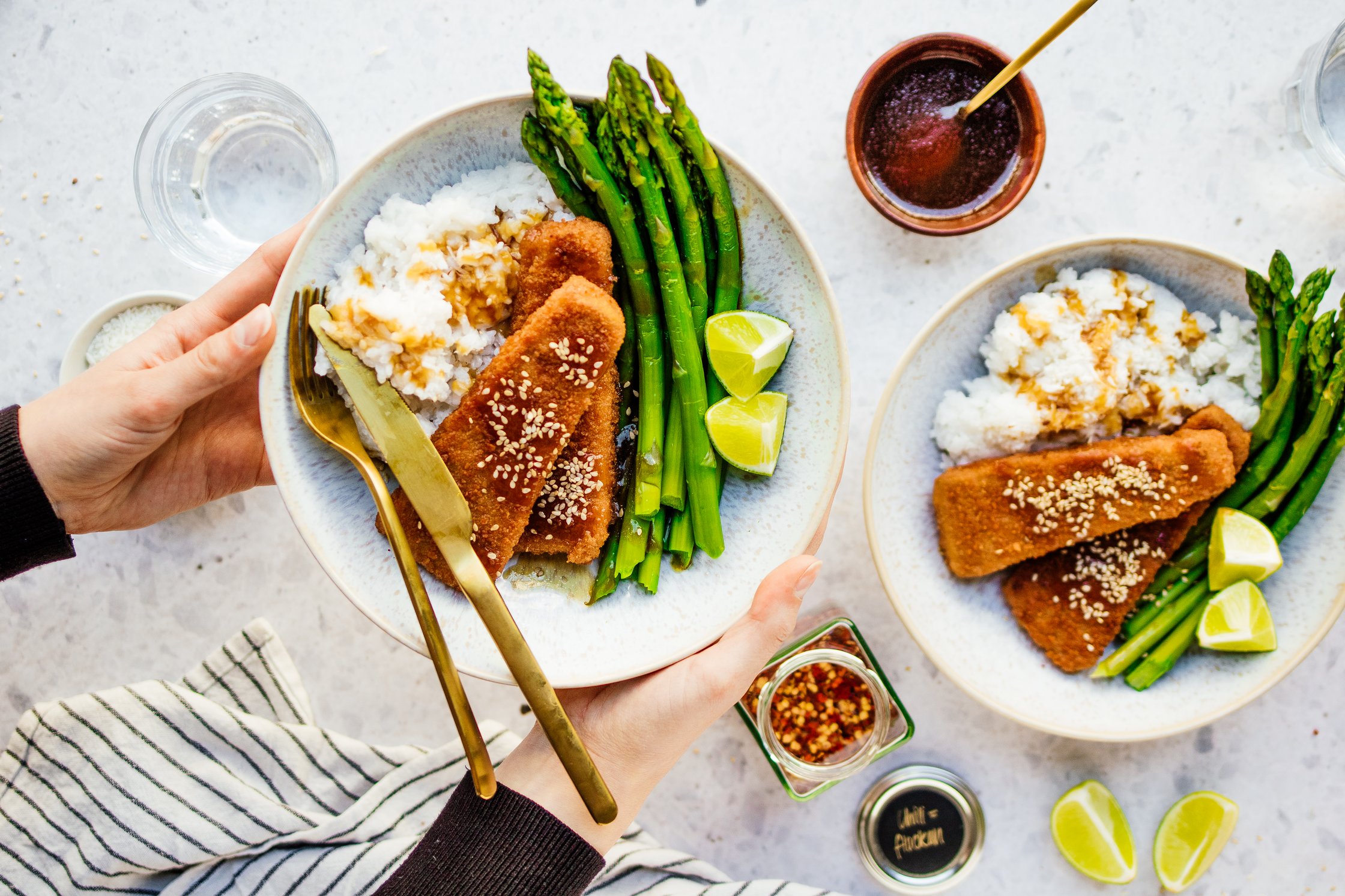 Zwei Teller mit Spargel, Reis und veganen Fisch Fillets, Soße und Besteck