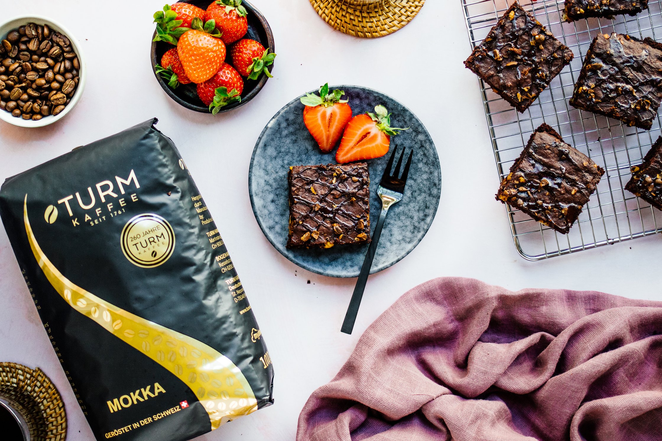 Vegane Espresso-Brownies auf einem Teller mit Erdbeeren und einer Gabel, Kaffee Verpackung