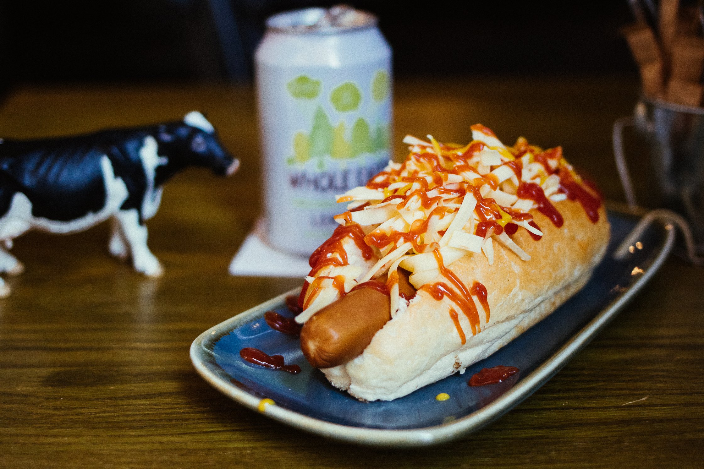 ein Hot Dog mit sehr viel Käse liegt auf einem blauen Teller