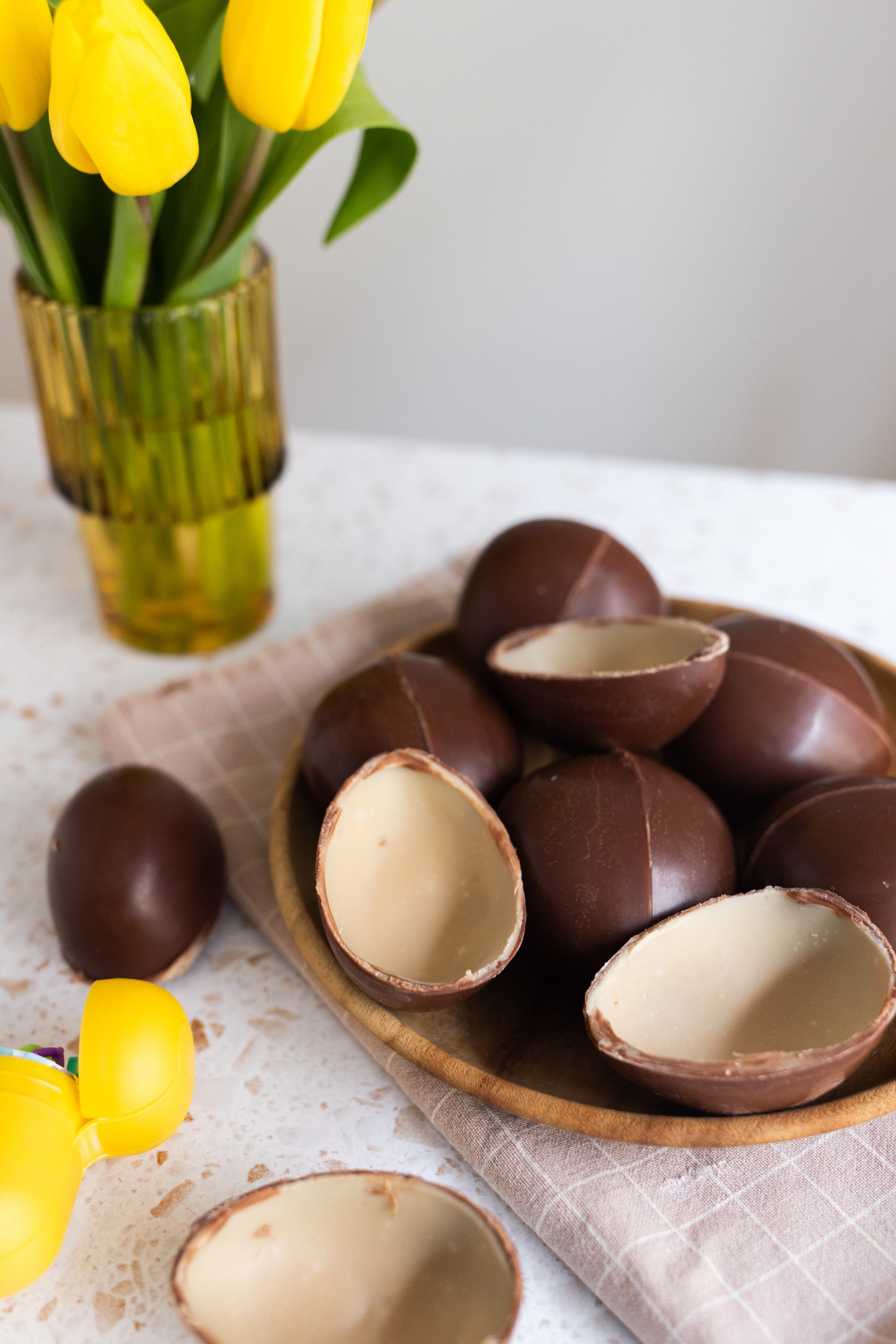 The finished chocolate eggs lie in a bowl with colorful tulips next to them.