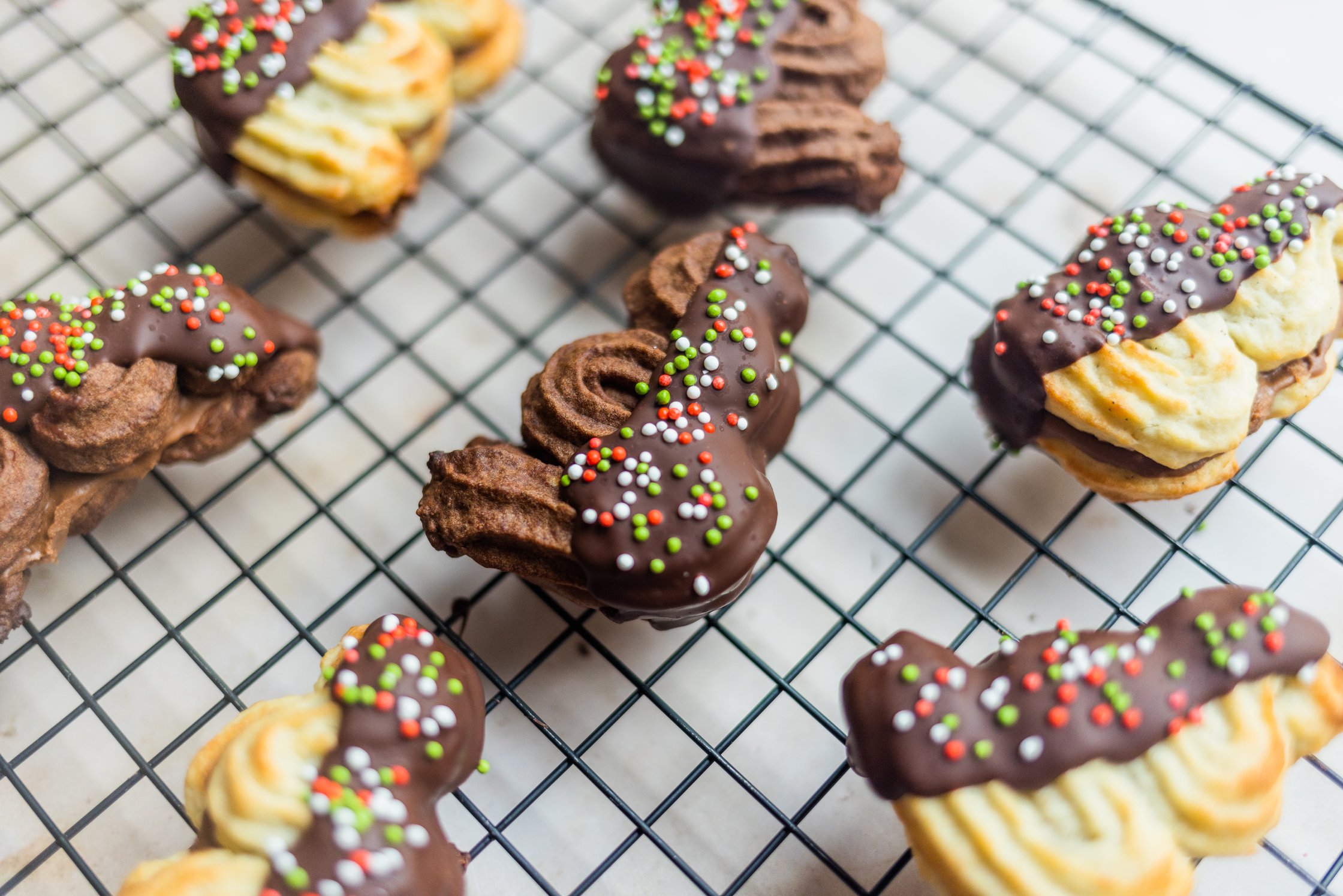 vegan spritz cookies lies on a grid, it is decorated with chocolate and colorful sprinkles