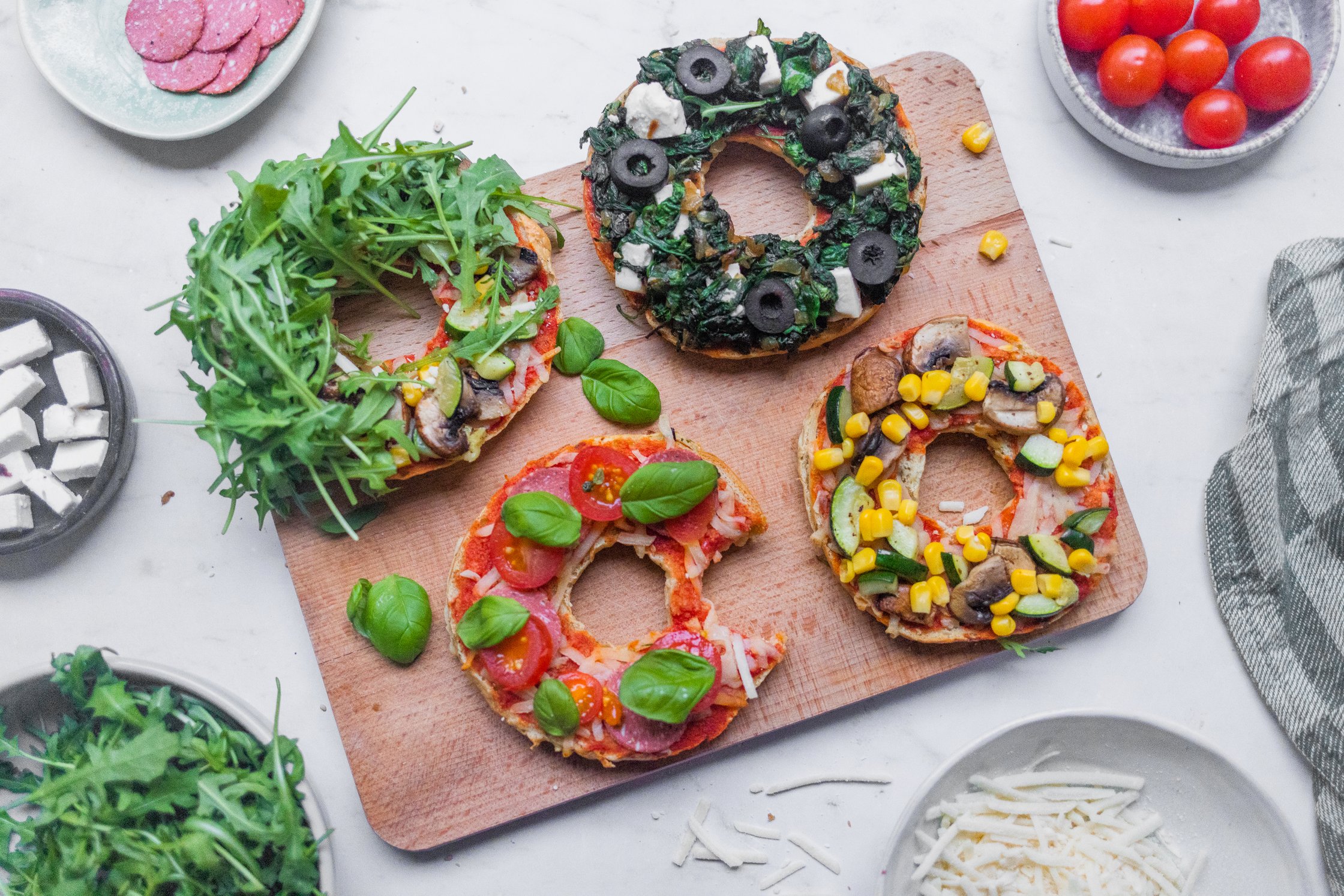 Vegane Pizzabagel mit verschiedenen Toppings auf einem Holzbrettchen.