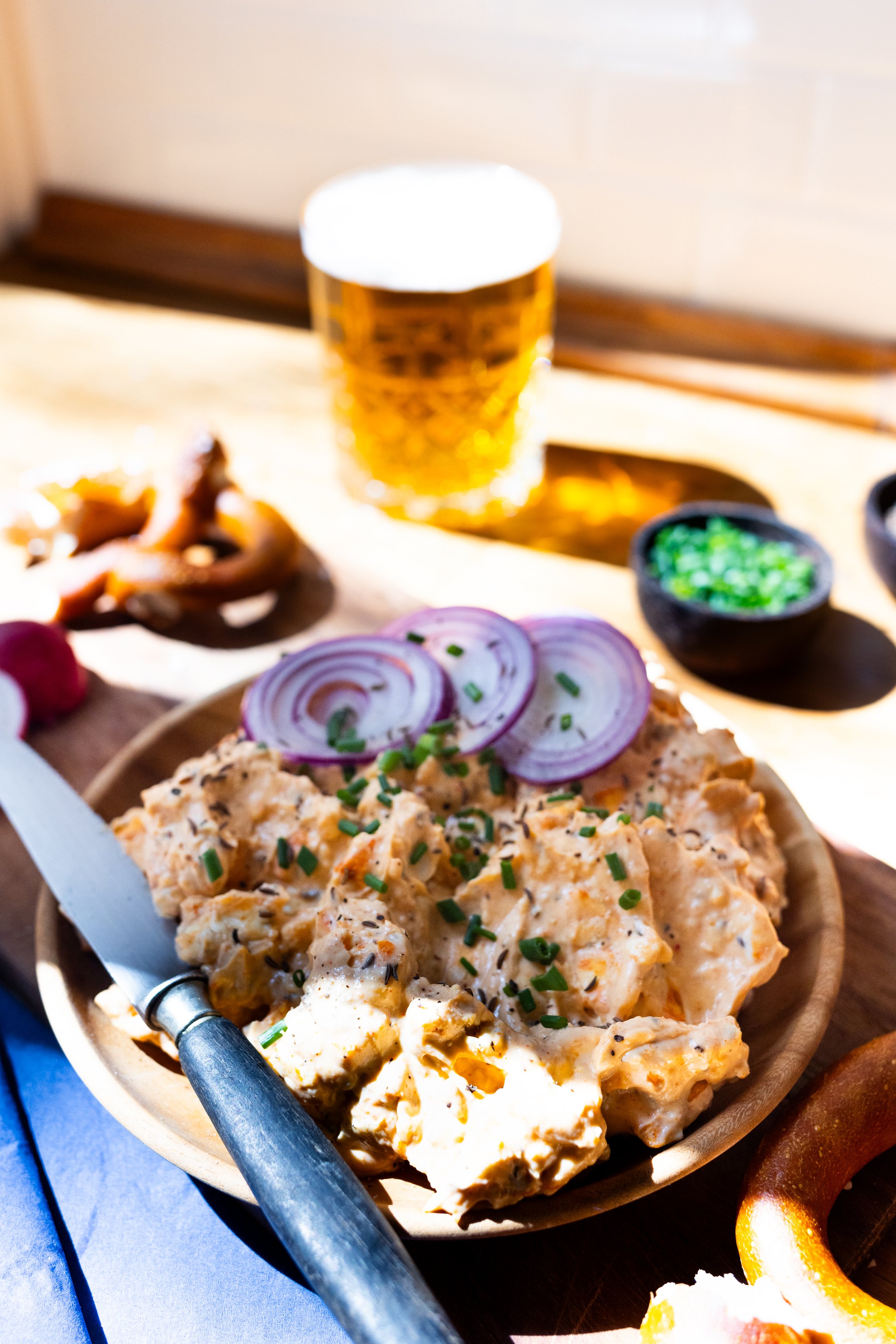 obazda on plate with knife, beer, pretzels, radishes in the background