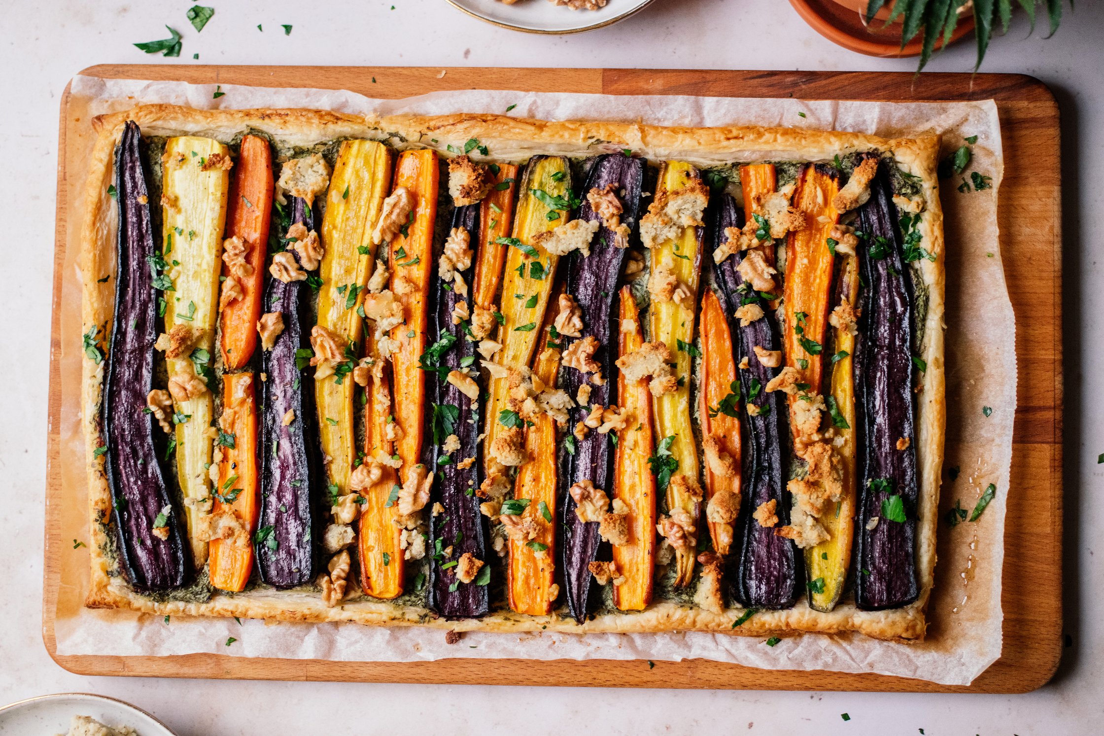 Möhrentarte mit Dinkel-Blätterteig und veganem Fetakäse serviert auf einem schneidebrett